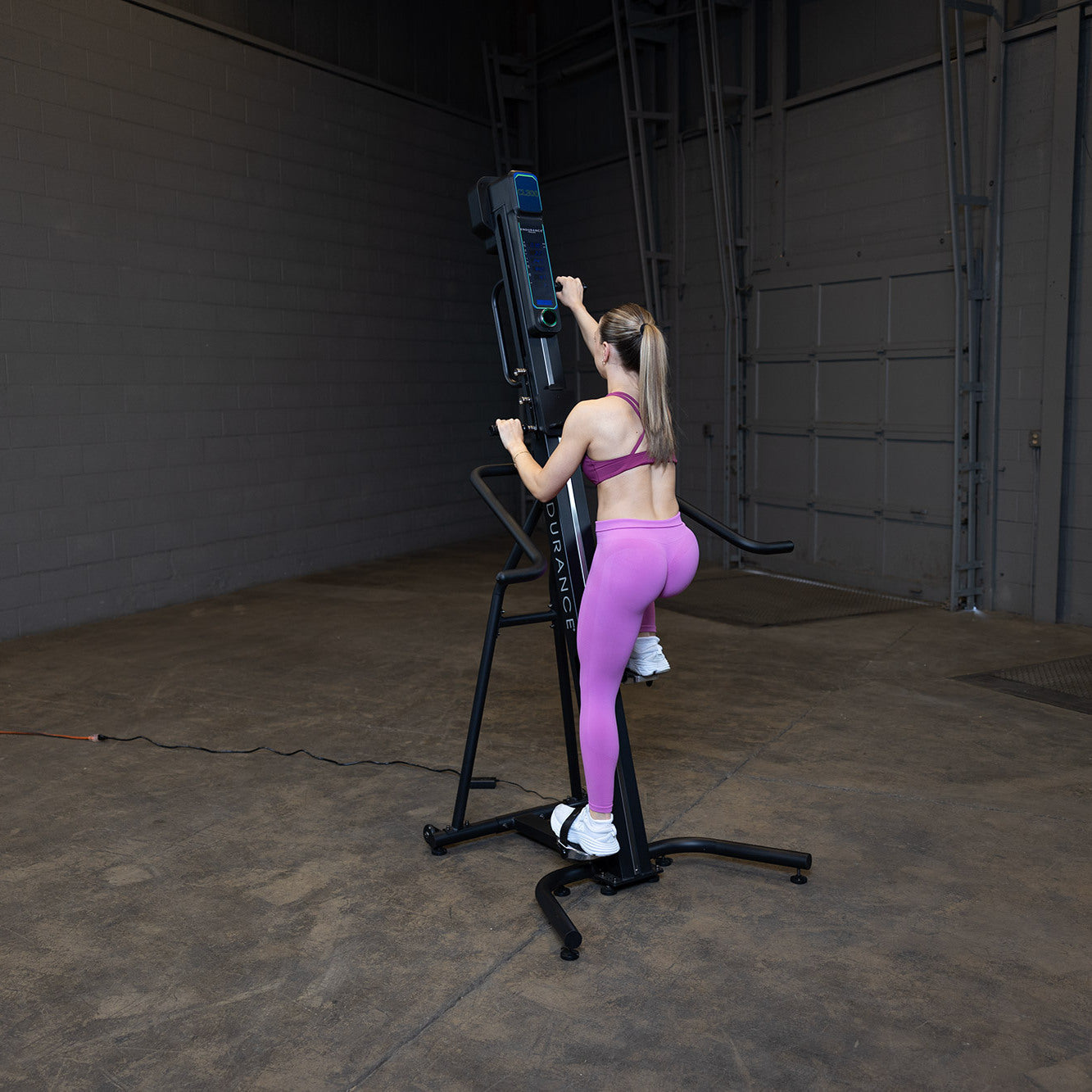 Woman using Body-Solid Endurance CL300 vertical climber for full-body low-impact cardio workout in home gym setting