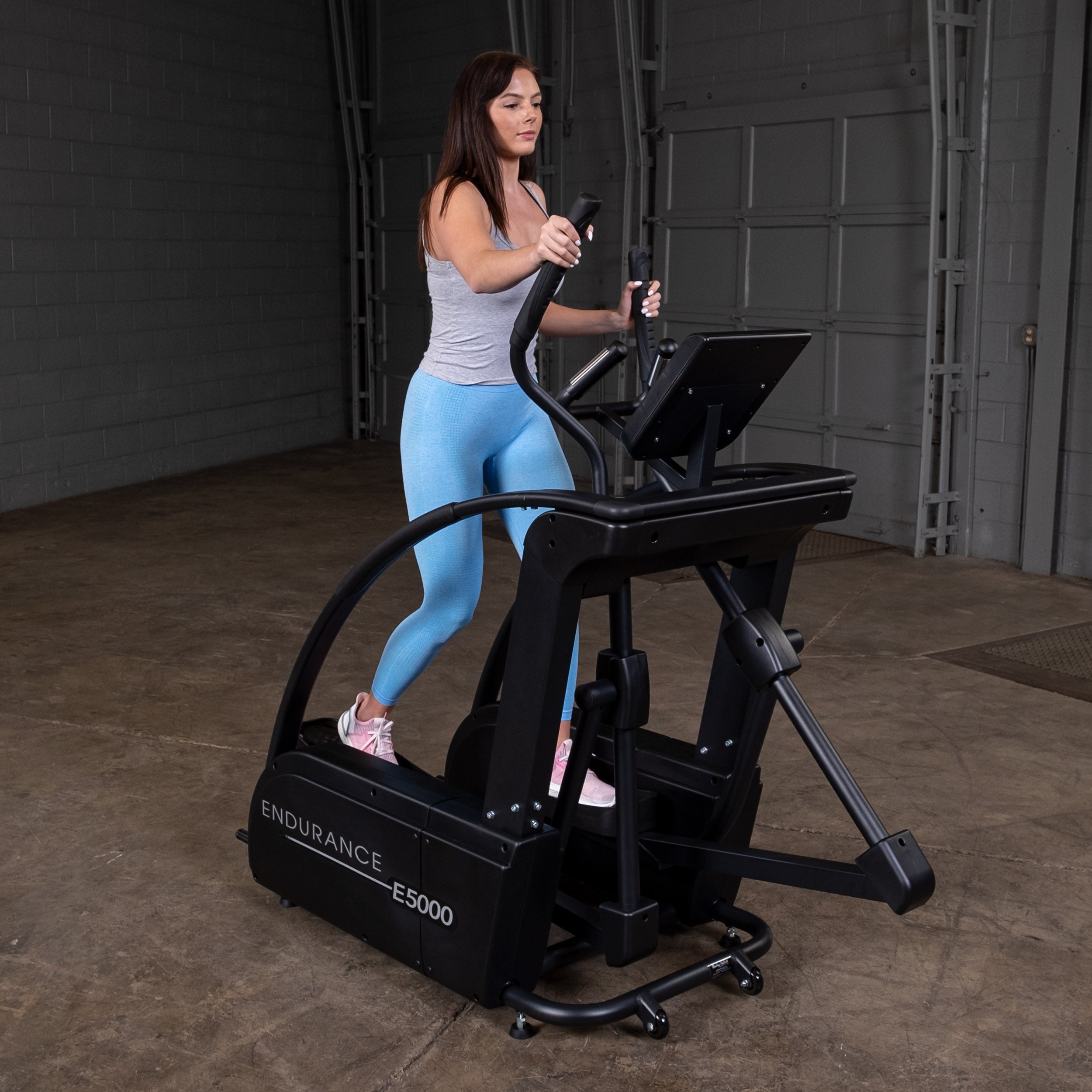 Woman using Body-Solid Endurance E5000 elliptical trainer in home gym setting showing low impact full body workout