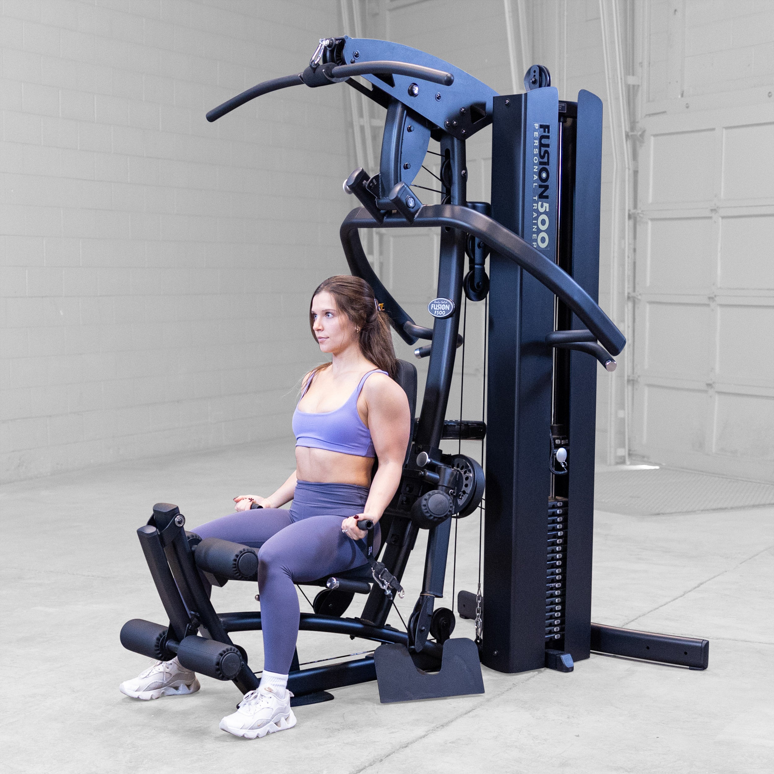 Person performing a seated bicep curl on the Body-Solid Fusion 500B Personal Trainer using the low pulleys and single handle attachments