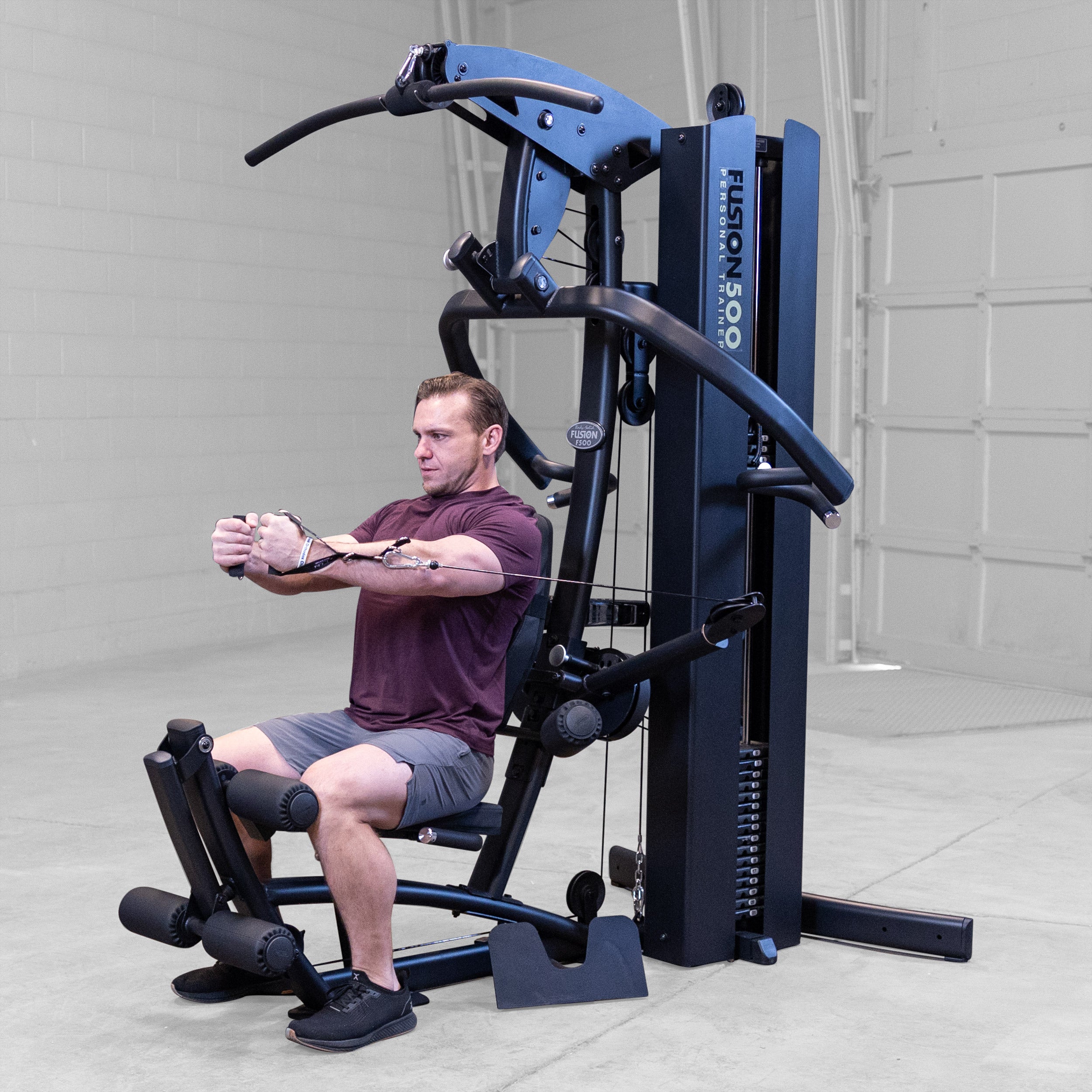Person performing a seated cable chest fly on the Body-Solid Fusion 500B Personal Trainer using the adjustable functional arms and single handle attachments