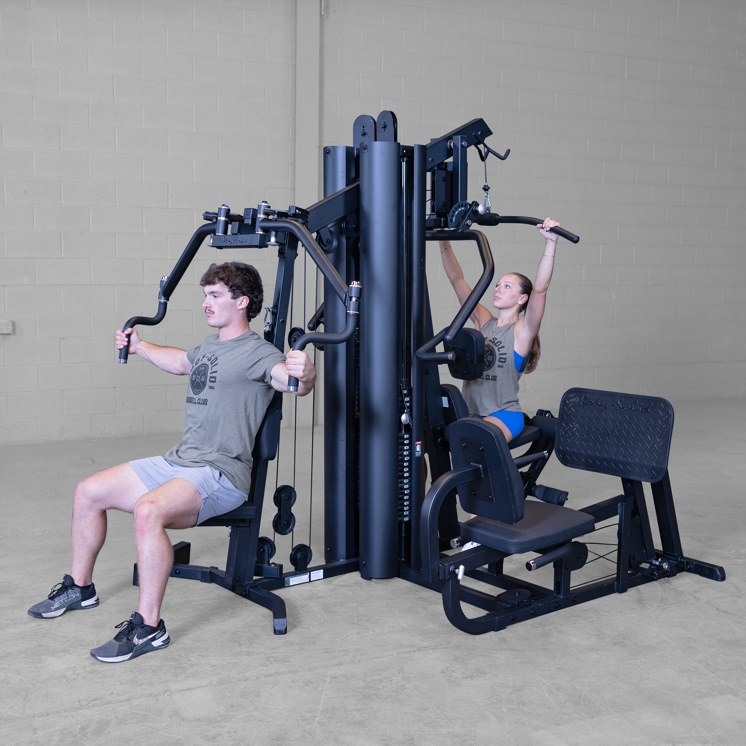 Two people performing chest press and lat pulldown exercises simultaneously on the Body-Solid G9B dual stack multi station home gym