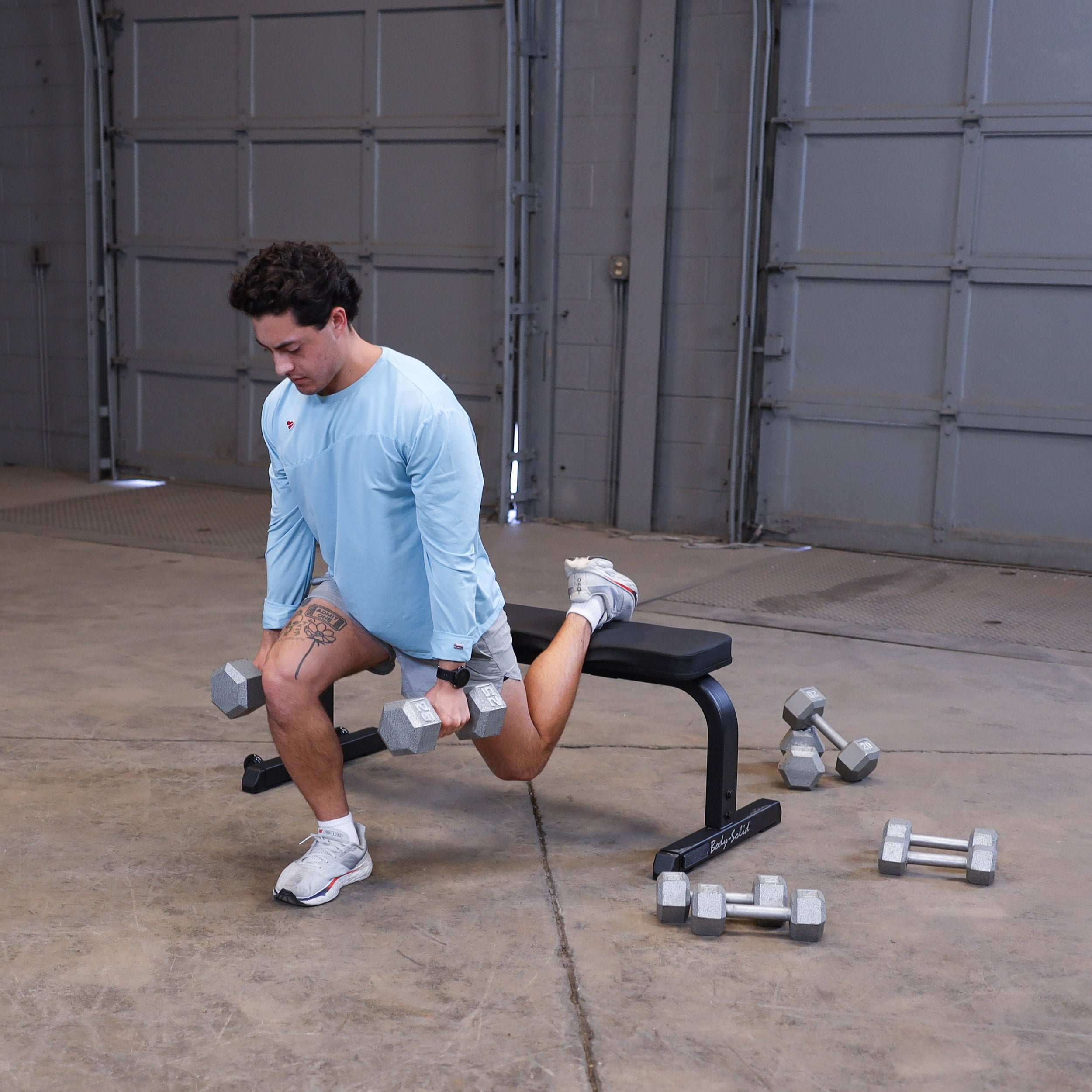 Person performing Bulgarian split squats using the Body-Solid GFB350B flat bench with dumbbells