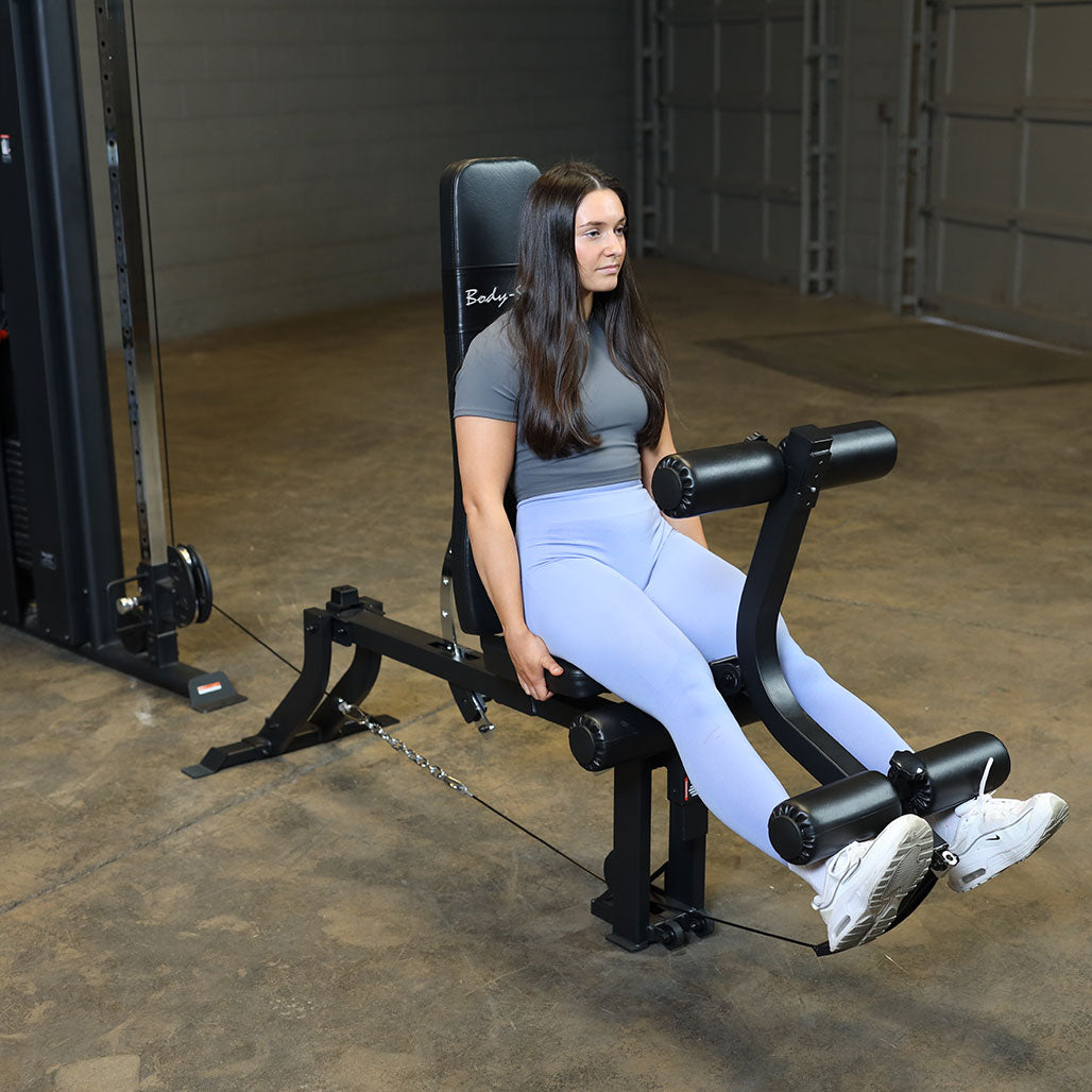 Person performing seated leg extensions on the Body-Solid GLEG leg extension curl bench attached to a cable machine for quadriceps training