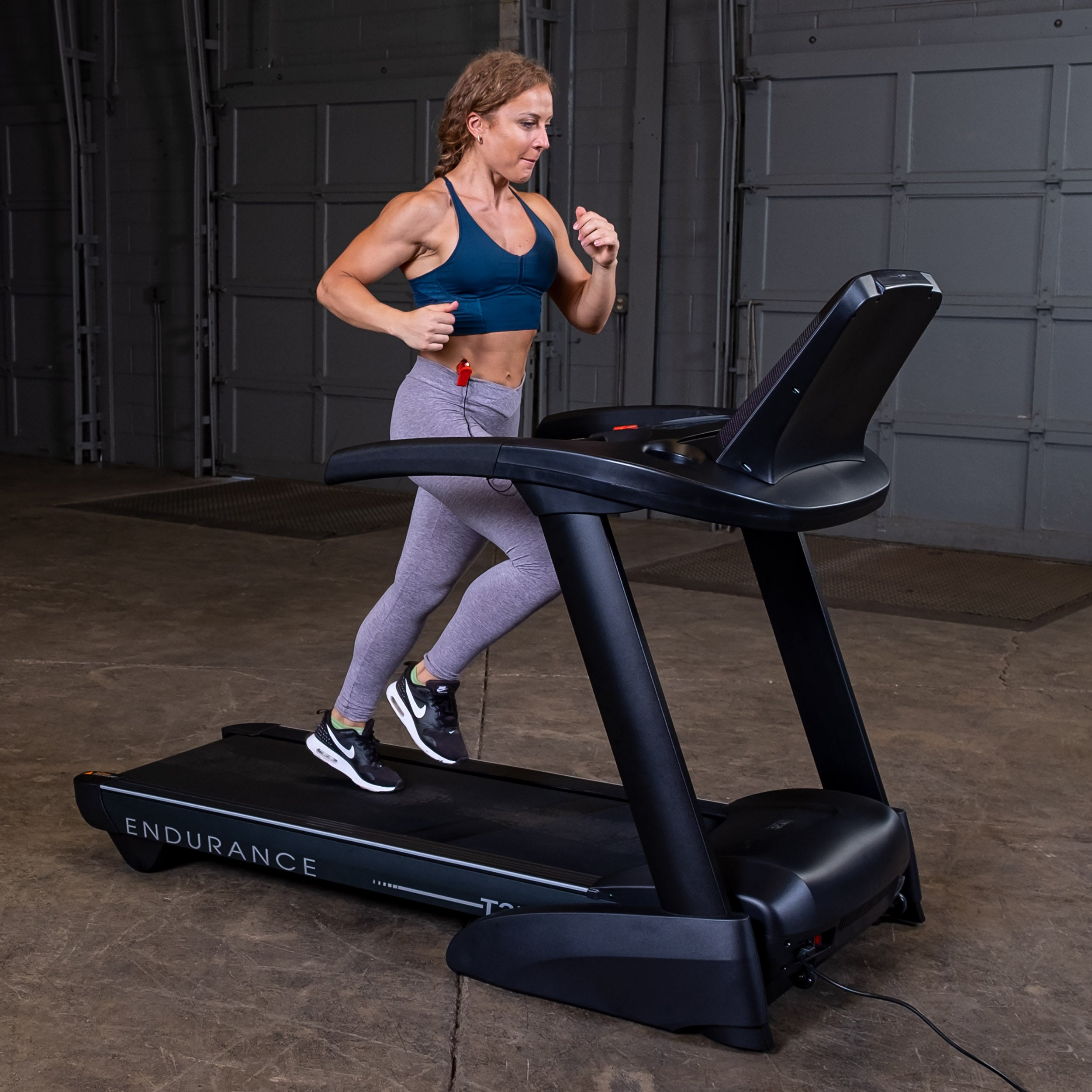 Woman running on Body-Solid Endurance T25 treadmill side view during home cardio workout
