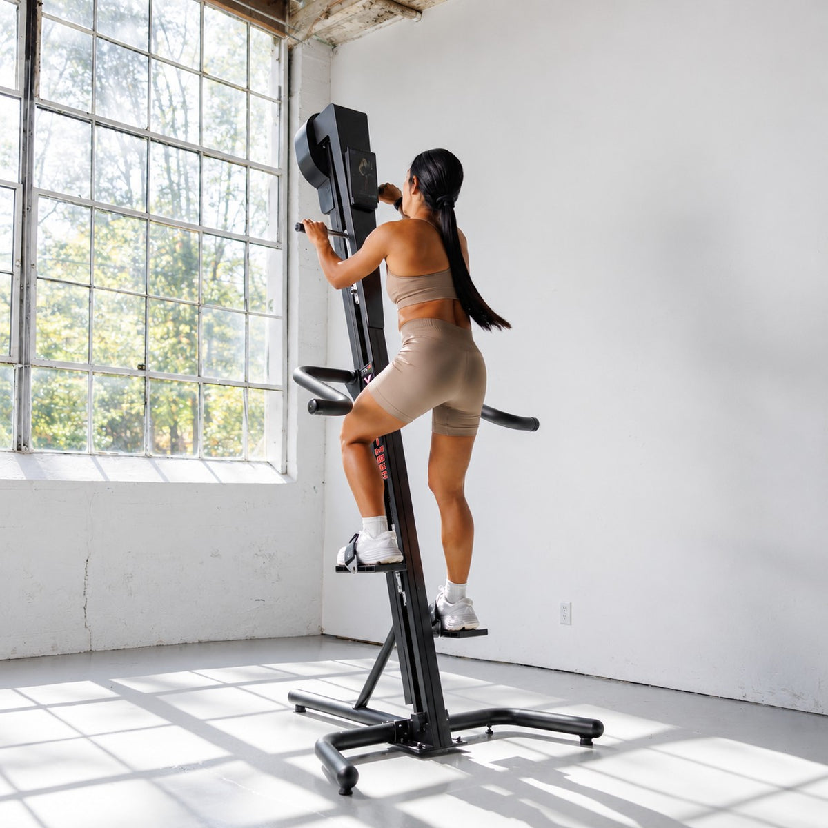 Woman using the VersaClimber TS-Magnetic vertical climber for a full-body cardio workout in a bright fitness studio