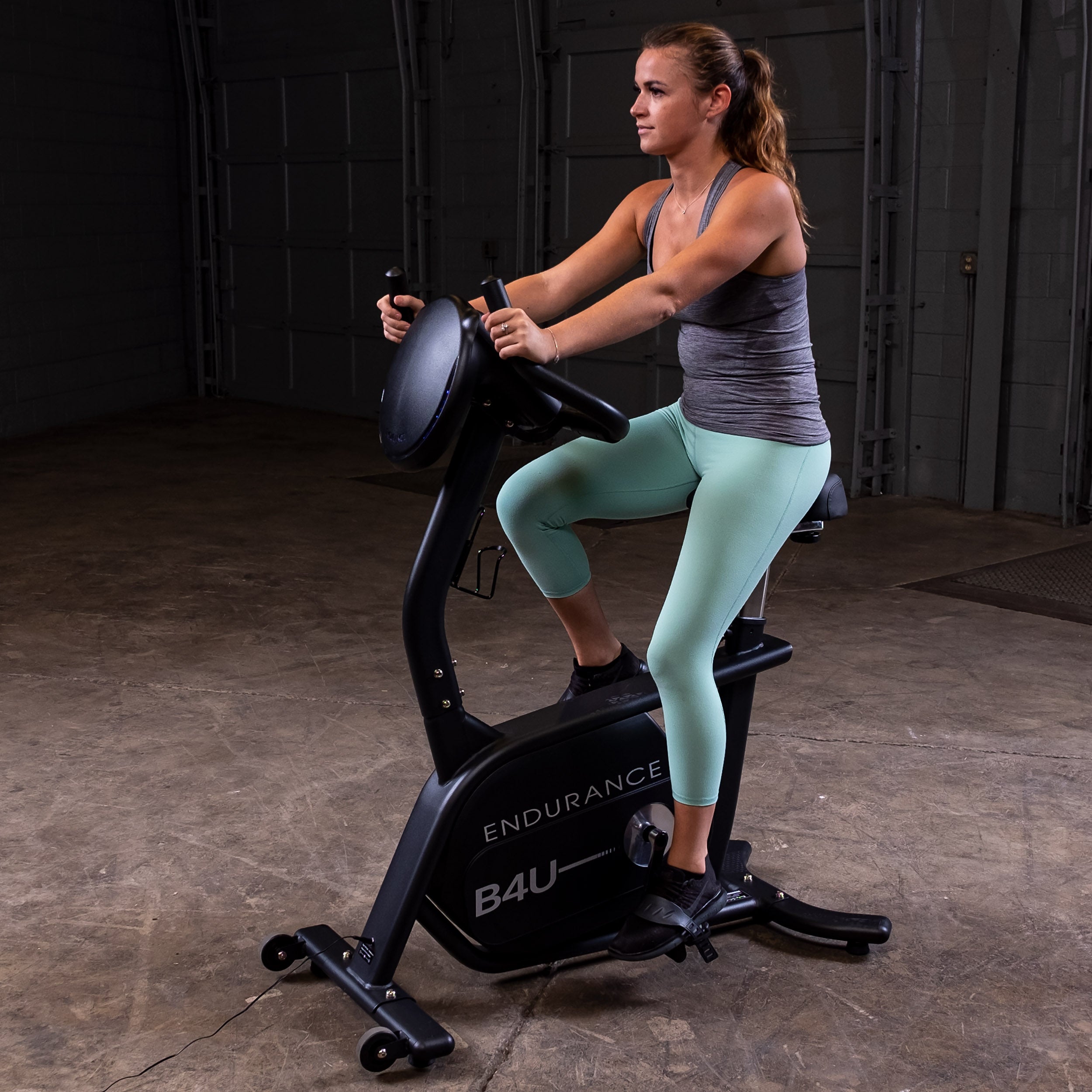 Woman using Body-Solid Endurance B4UB upright exercise bike during home cardio workout