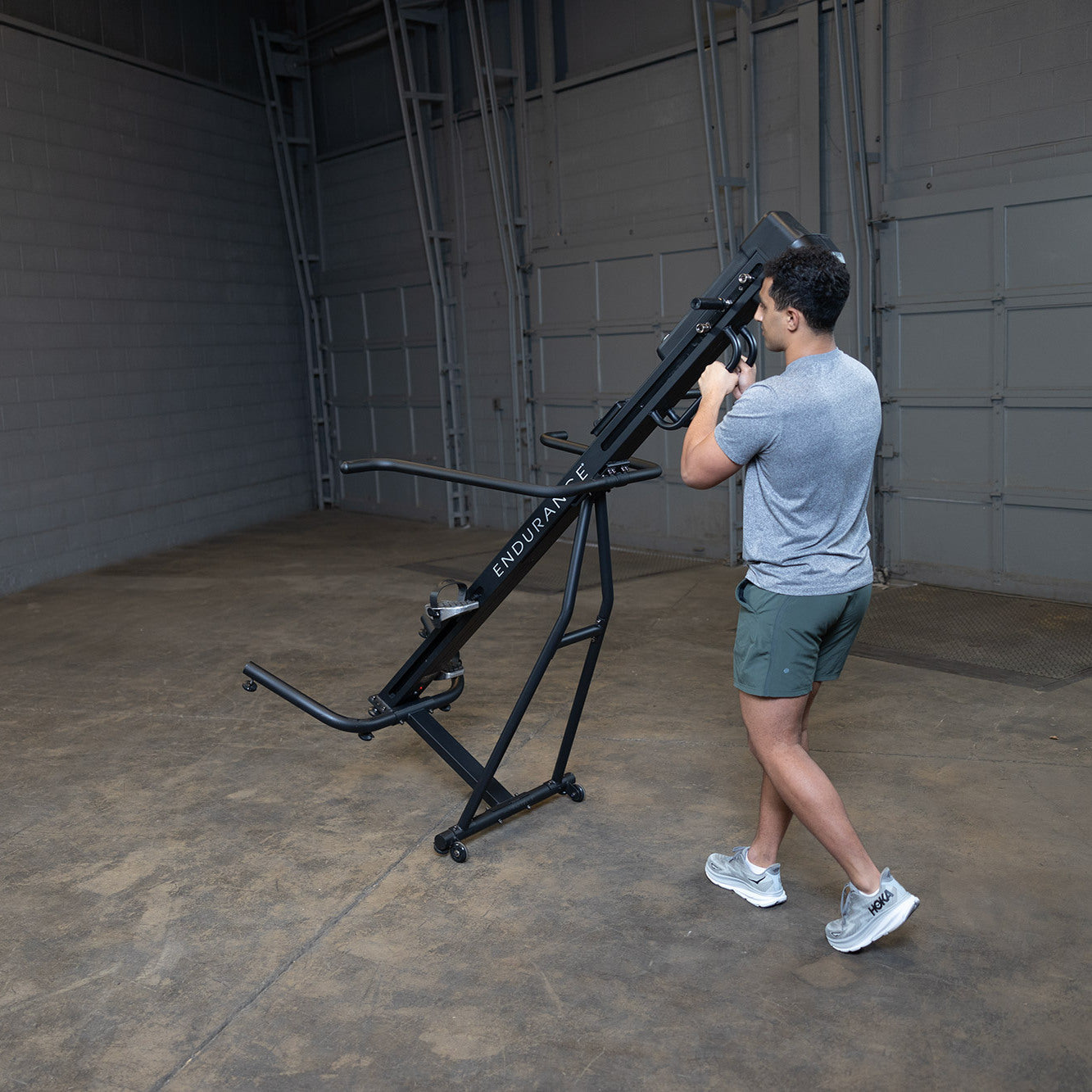 Man moving Body-Solid Endurance CL300 vertical climber using transport wheels for easy repositioning in home gym setting
