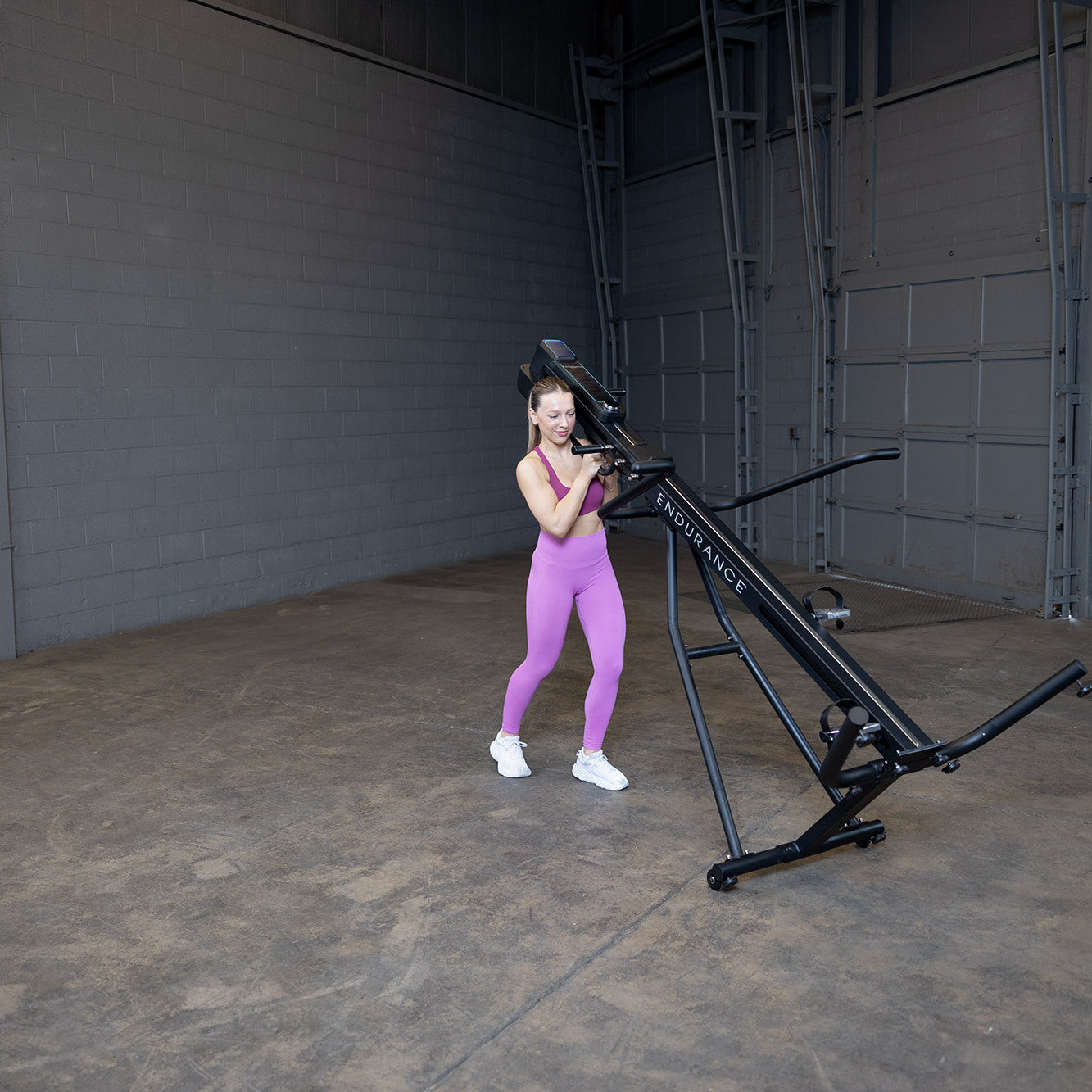Woman moving Body-Solid Endurance CL300 vertical climber using transport wheels for easy repositioning in home gym setting