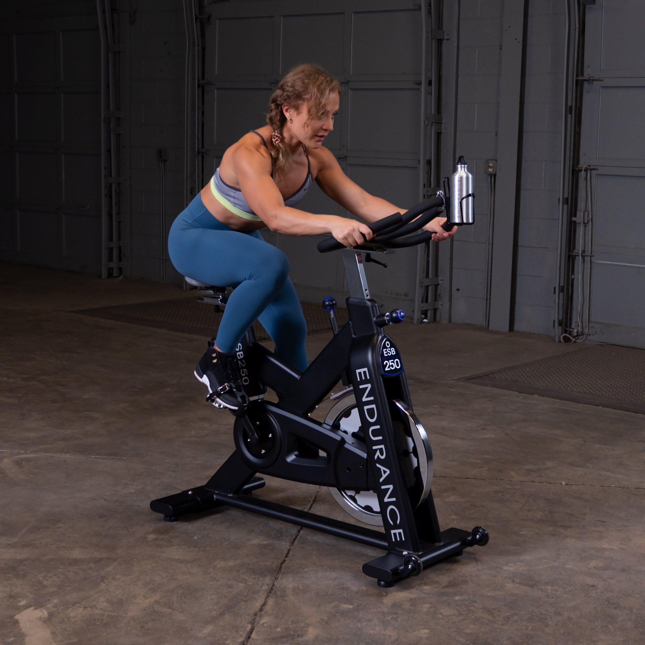 Person riding the Body-Solid Endurance ESB250 indoor training cycle during a cardio workout demonstrating its smooth belt drive and adjustable riding position