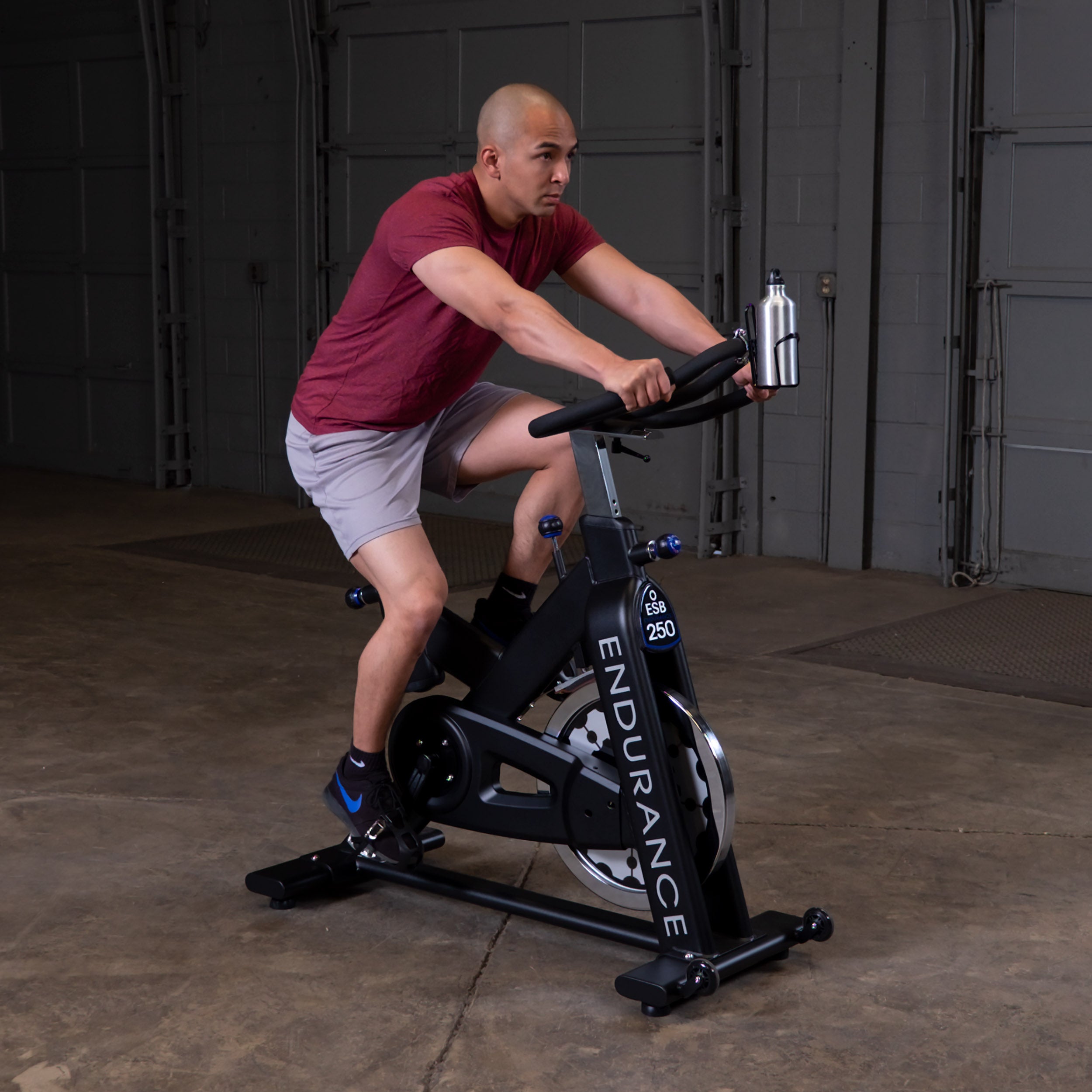 Person riding the Body-Solid Endurance ESB250 indoor training cycle in a standing position demonstrating high-intensity cardio training
