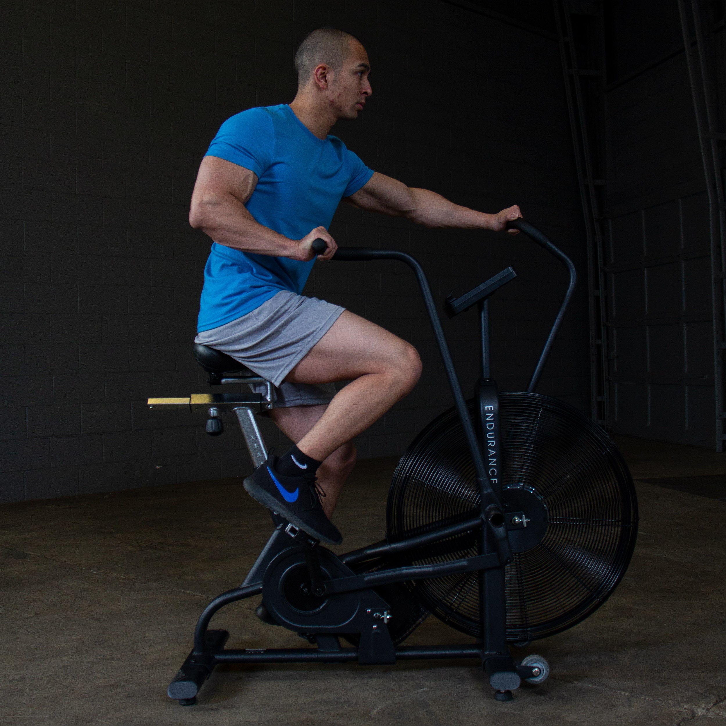 Athlete using the Body-Solid Endurance FB300B fan bike during a cardio workout, shown from the side to highlight the moving handlebars and air resistance fan