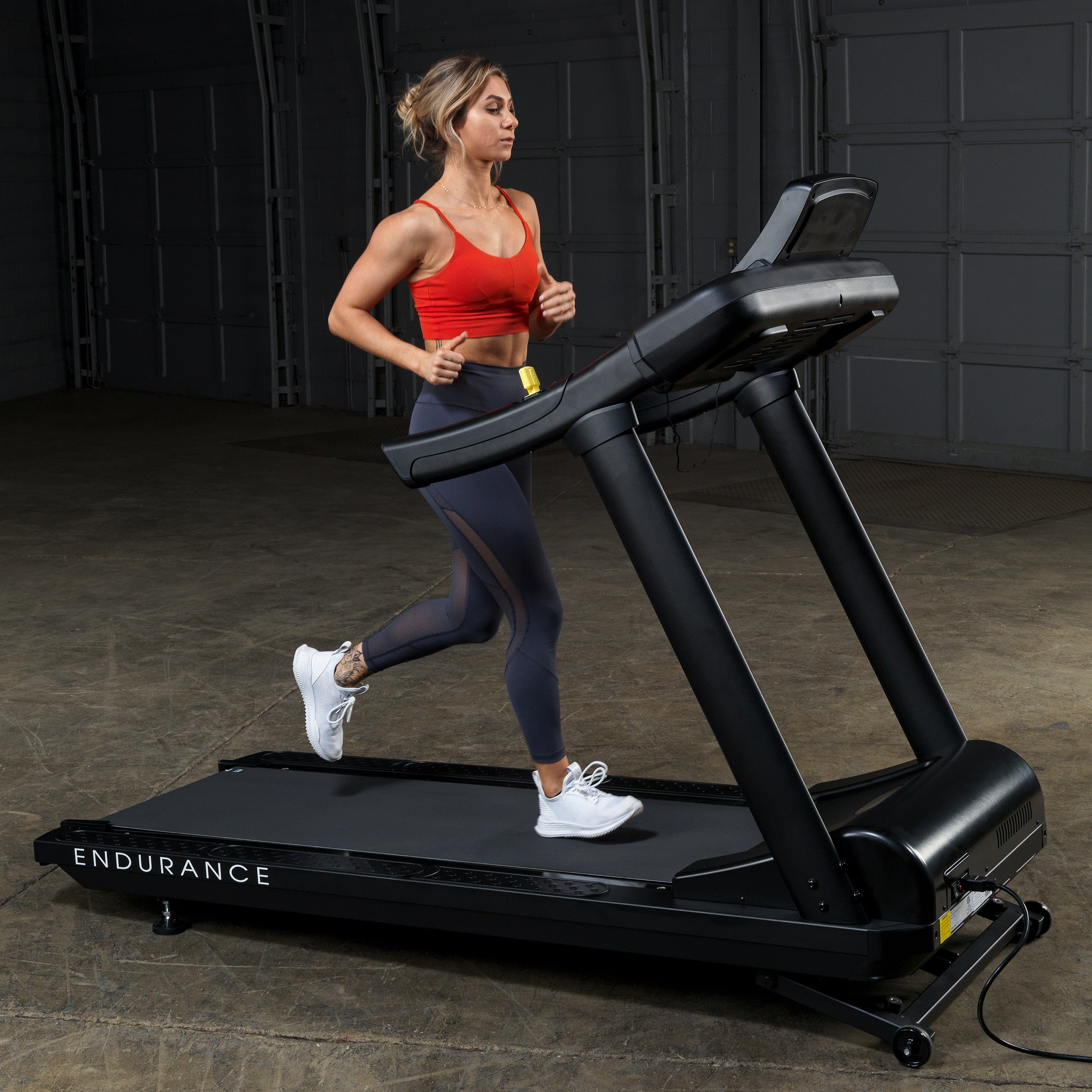 Woman running on Body-Solid Endurance T150 commercial treadmill in gym setting