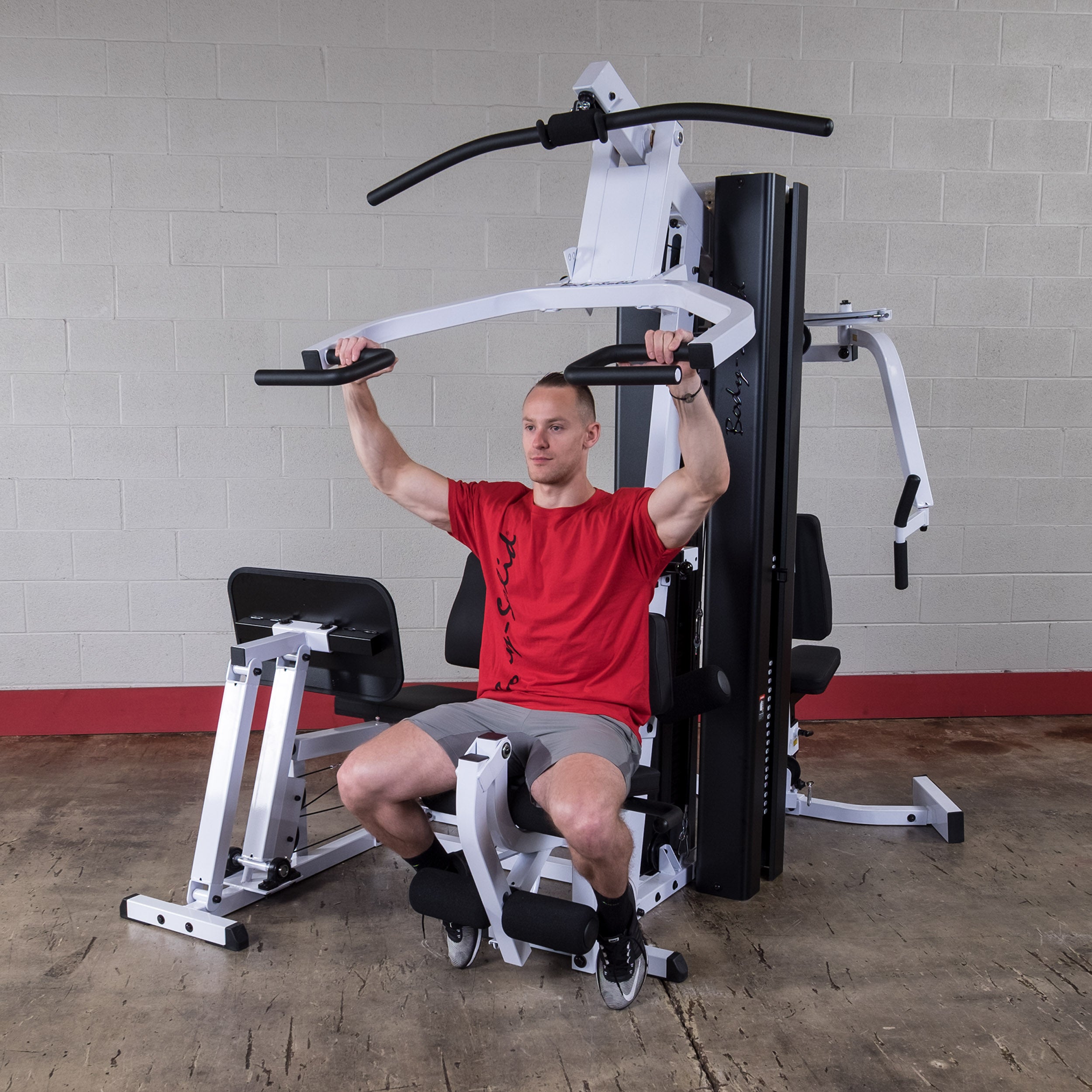 Person performing shoulder press exercises on the Body-Solid EXM3000LPS dual stack multi-station gym