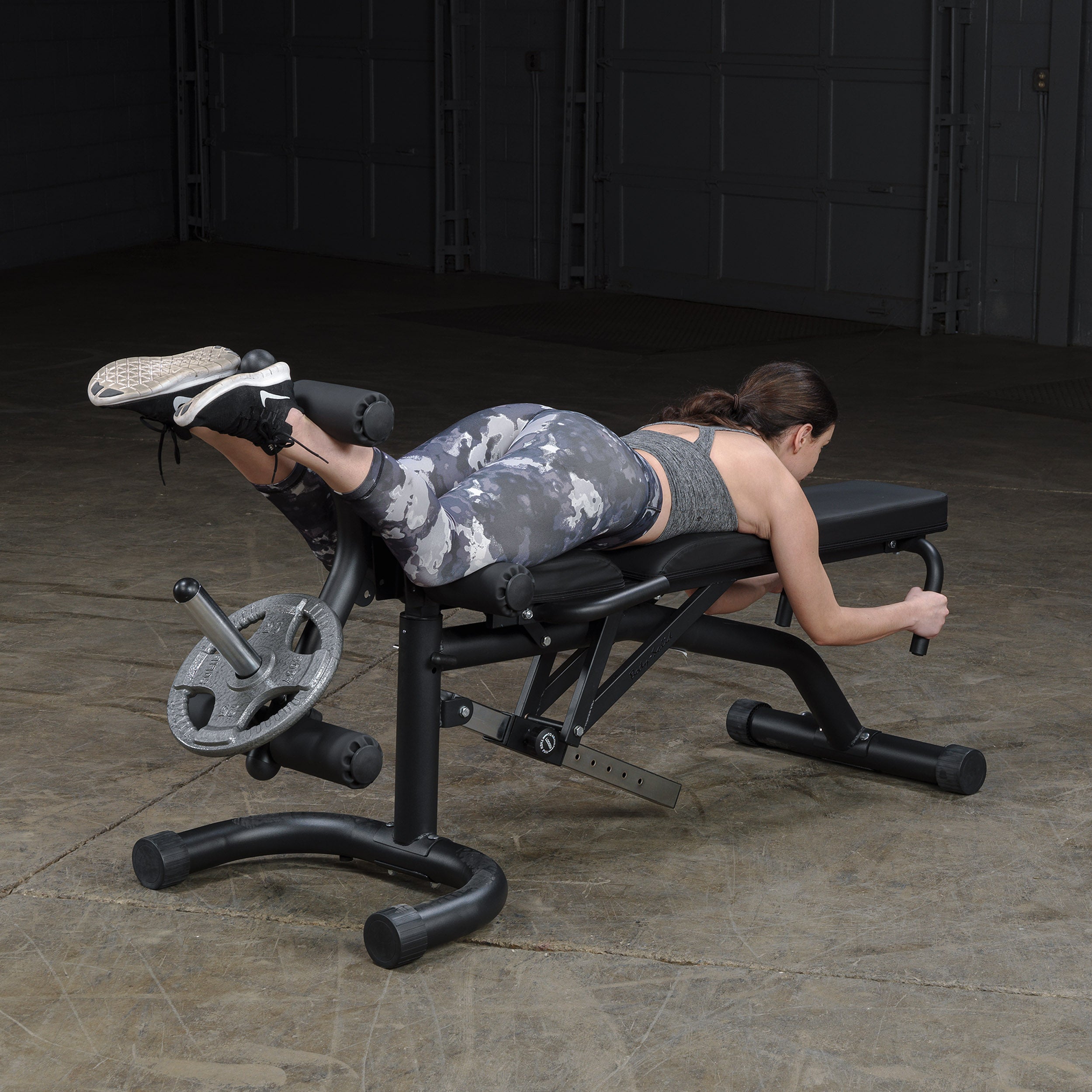 Person performing lying leg curls on the Body-Solid FID46 leverage flat incline decline bench with integrated leg developer