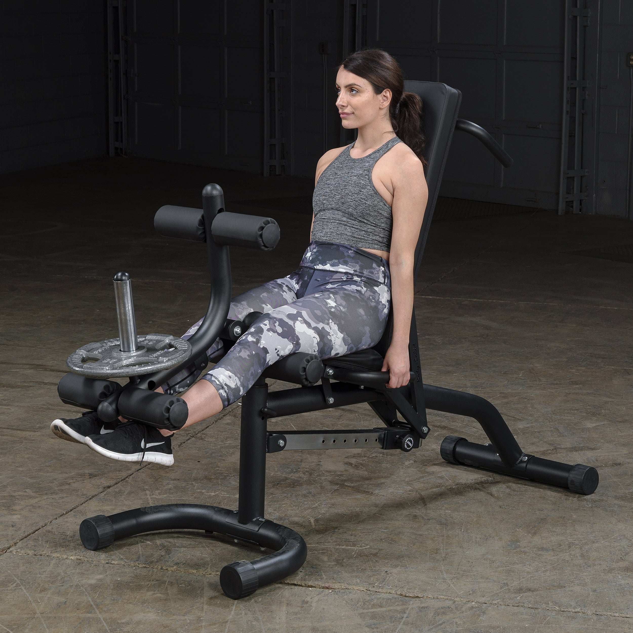 Person performing seated leg extensions on the Body-Solid FID46 leverage flat incline decline bench with integrated leg developer