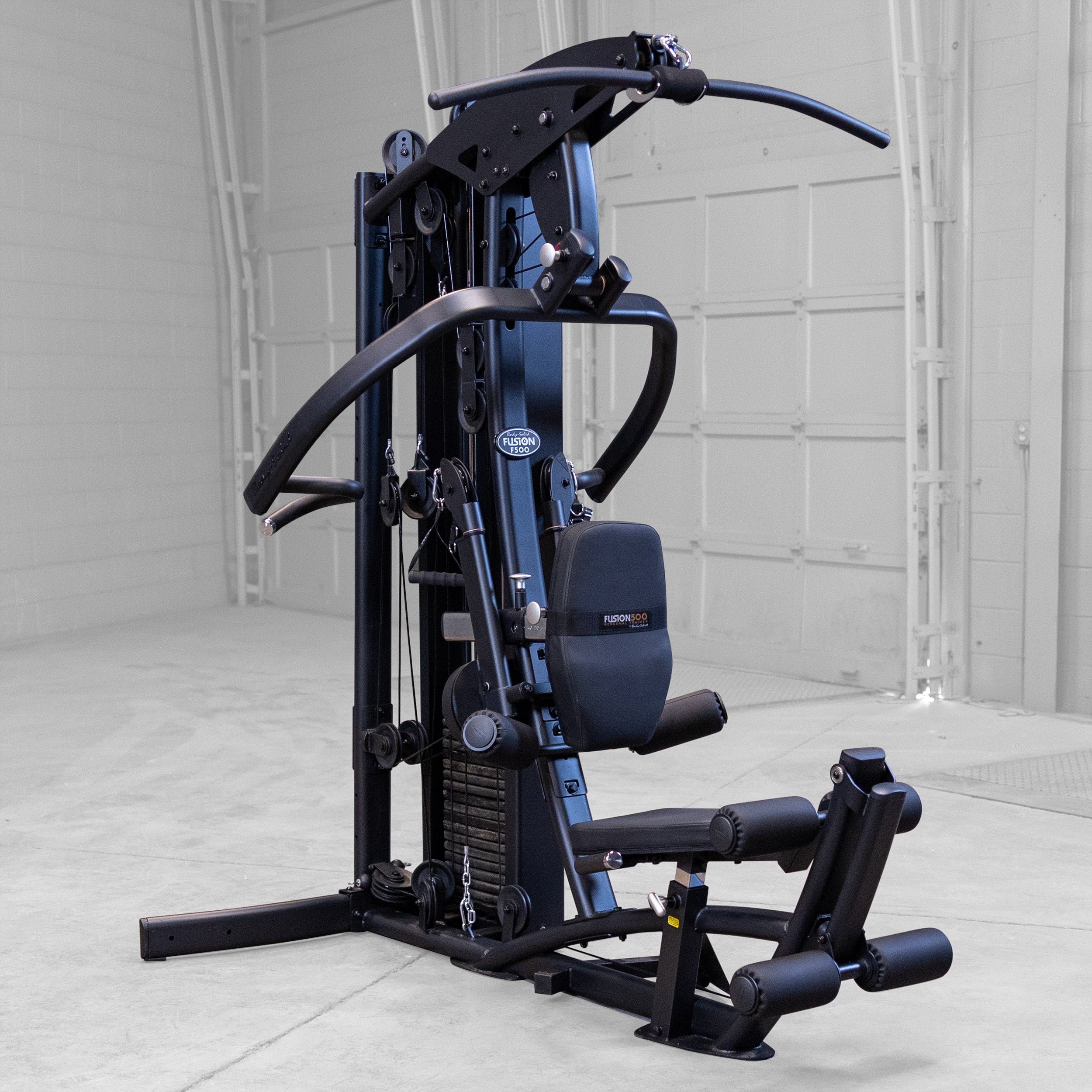 Body-Solid Fusion 500B Personal Trainer all-in-one home gym shown in a modern gym setting with articulating press arms, lat pulldown station, adjustable seat, and integrated weight stack