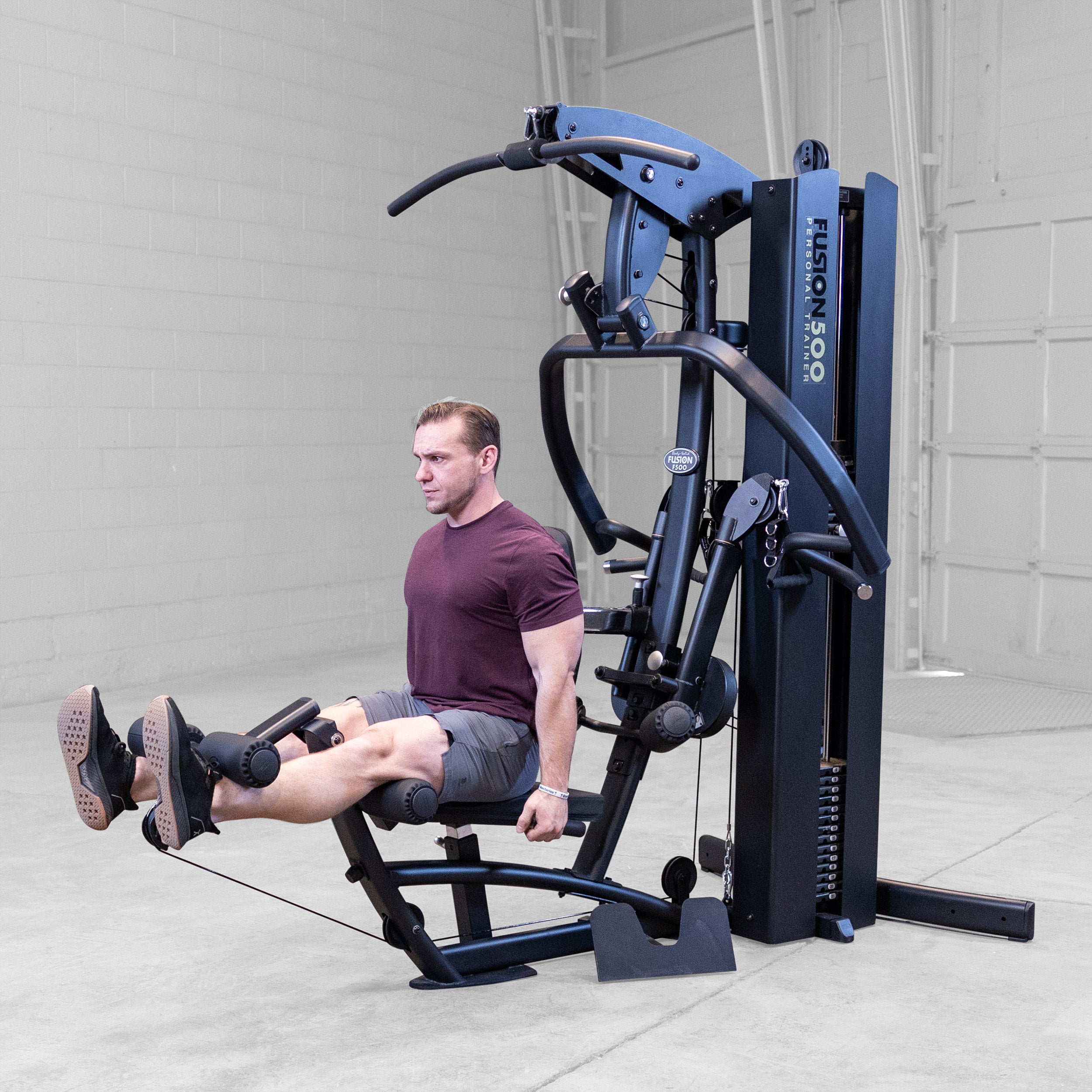 Person performing a leg extension on the Body-Solid Fusion 500B Personal Trainer using the leg developer and adjustable seat