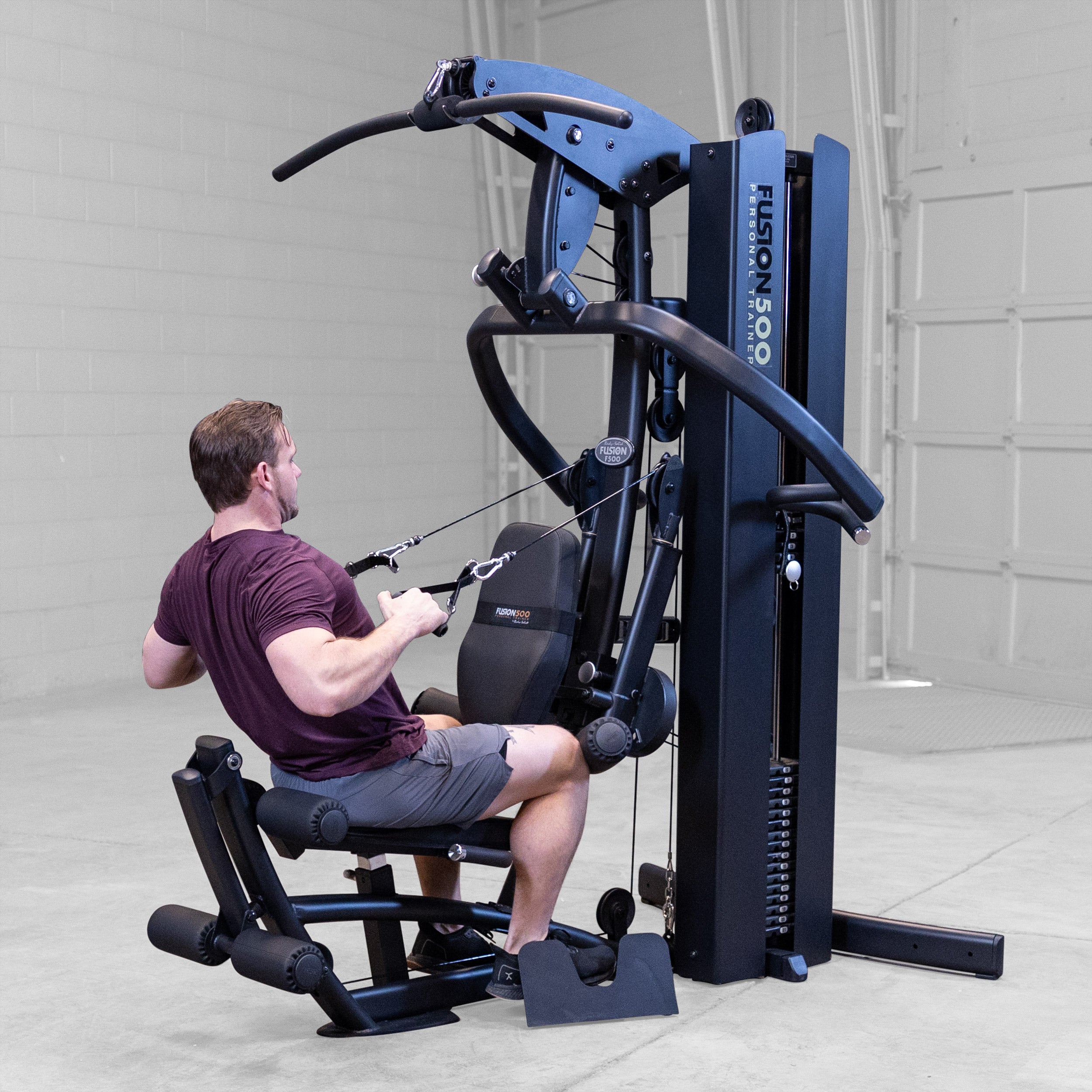 Person performing a seated cable row on the Body-Solid Fusion 500B Personal Trainer using the adjustable functional arms and single handle attachments