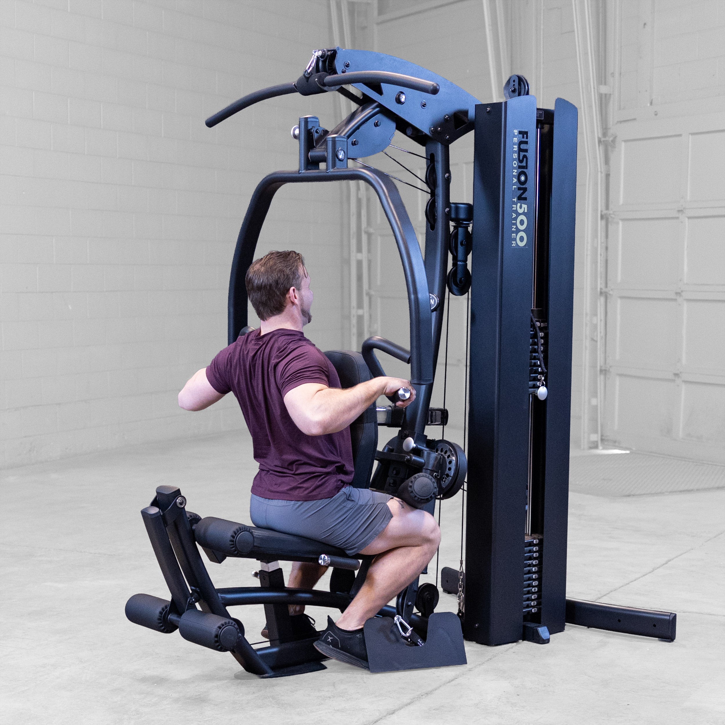 Person performing a seated row exercise on the Body-Solid Fusion 500B Personal Trainer using the articulating press arms and adjustable seat