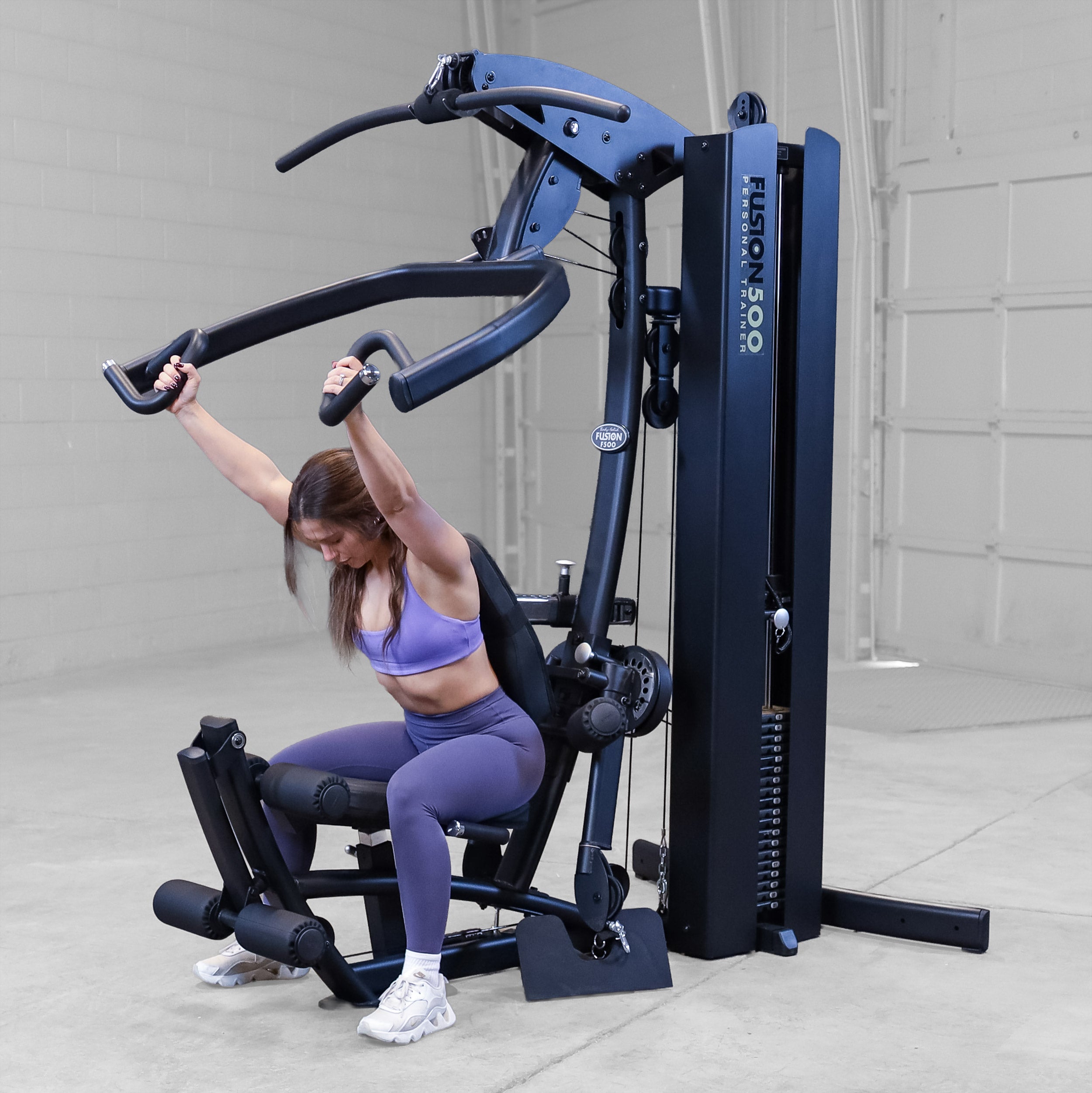 Person performing a shoulder press exercise on the Body-Solid Fusion 500B Personal Trainer using the articulating press arms and adjustable seat