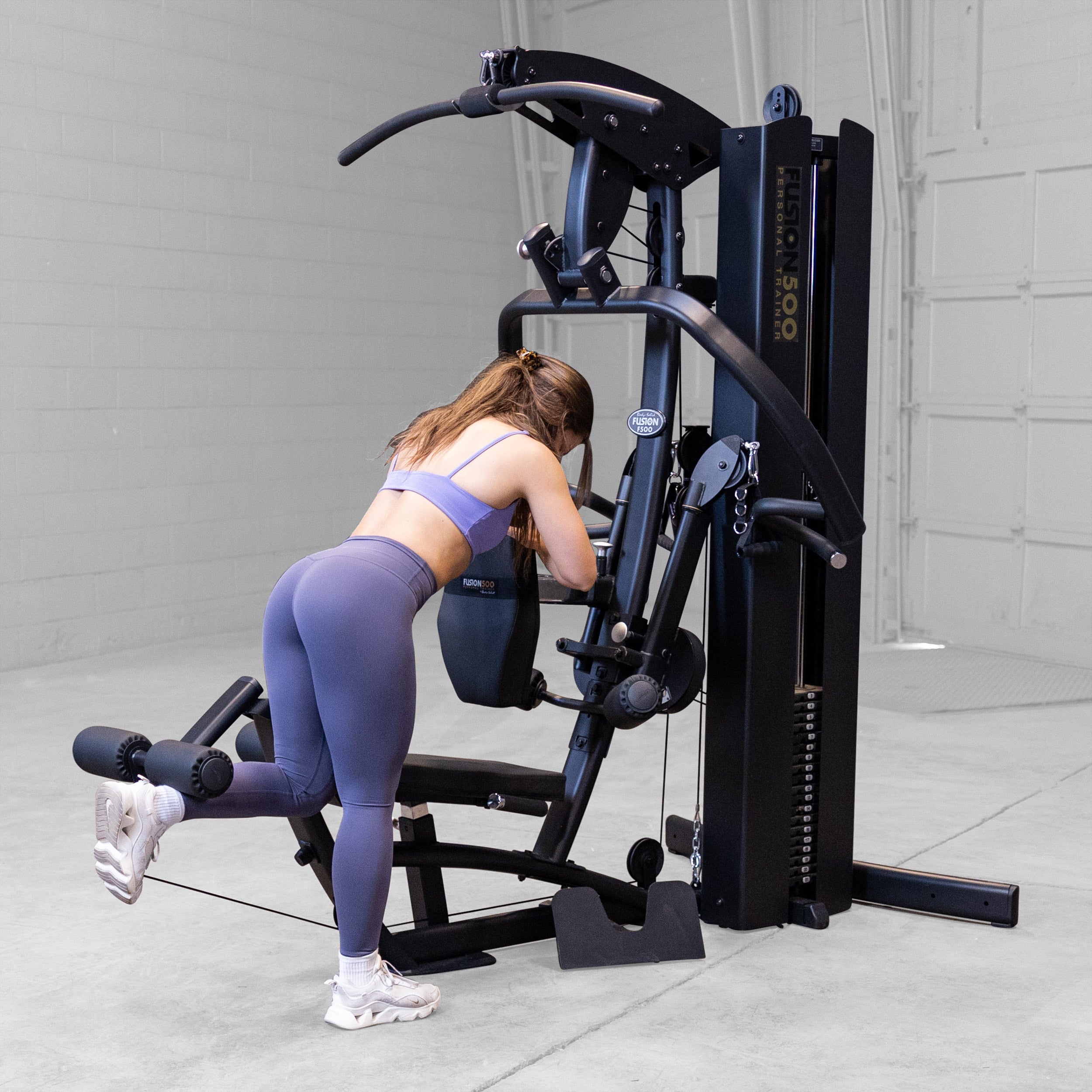 Person performing a standing leg curl on the Body-Solid Fusion 500B Personal Trainer using the leg developer and adjustable support pad