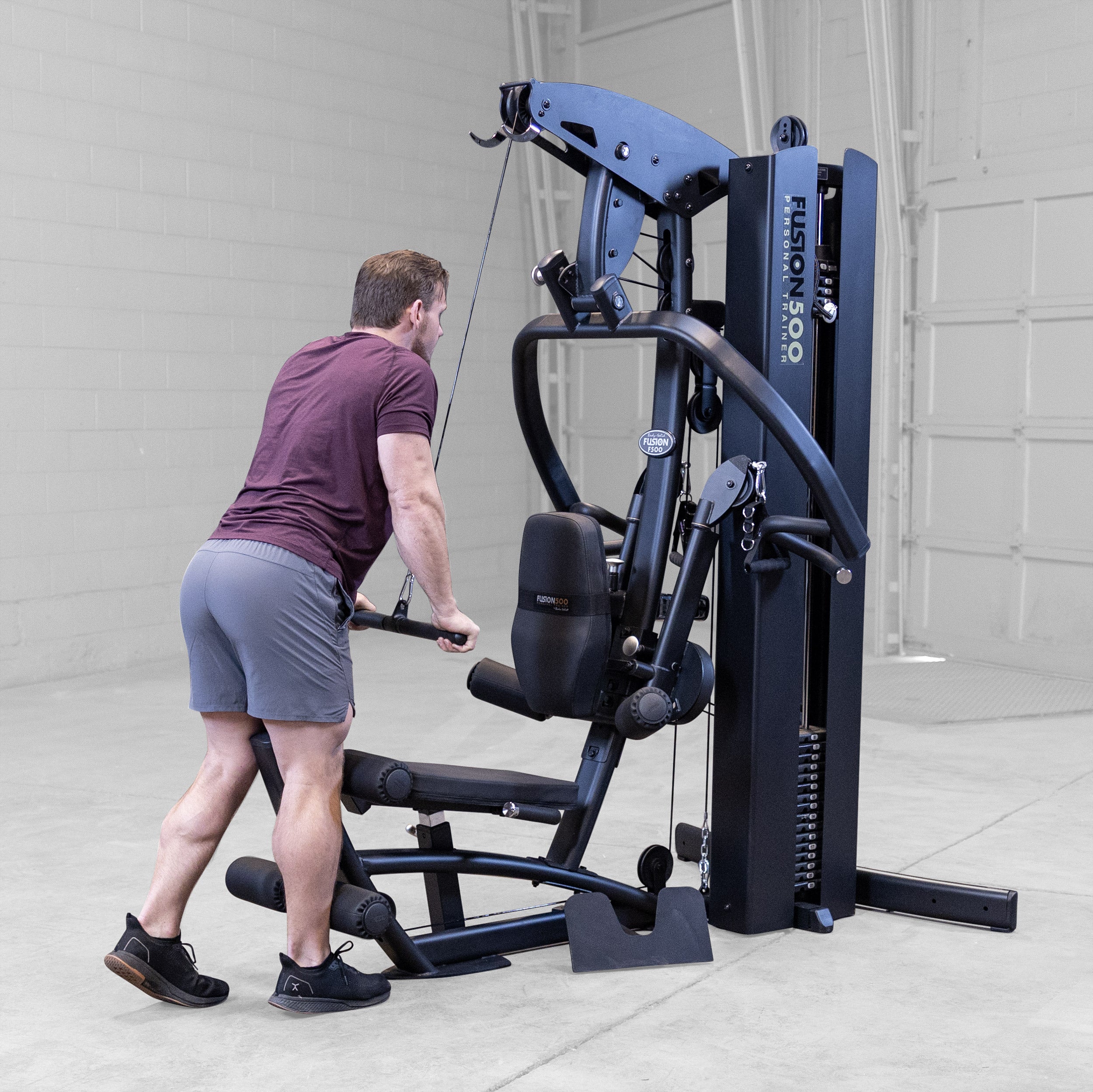 Person performing a standing triceps pressdown on the Body-Solid Fusion 500B Personal Trainer using the high pulley and straight bar attachment