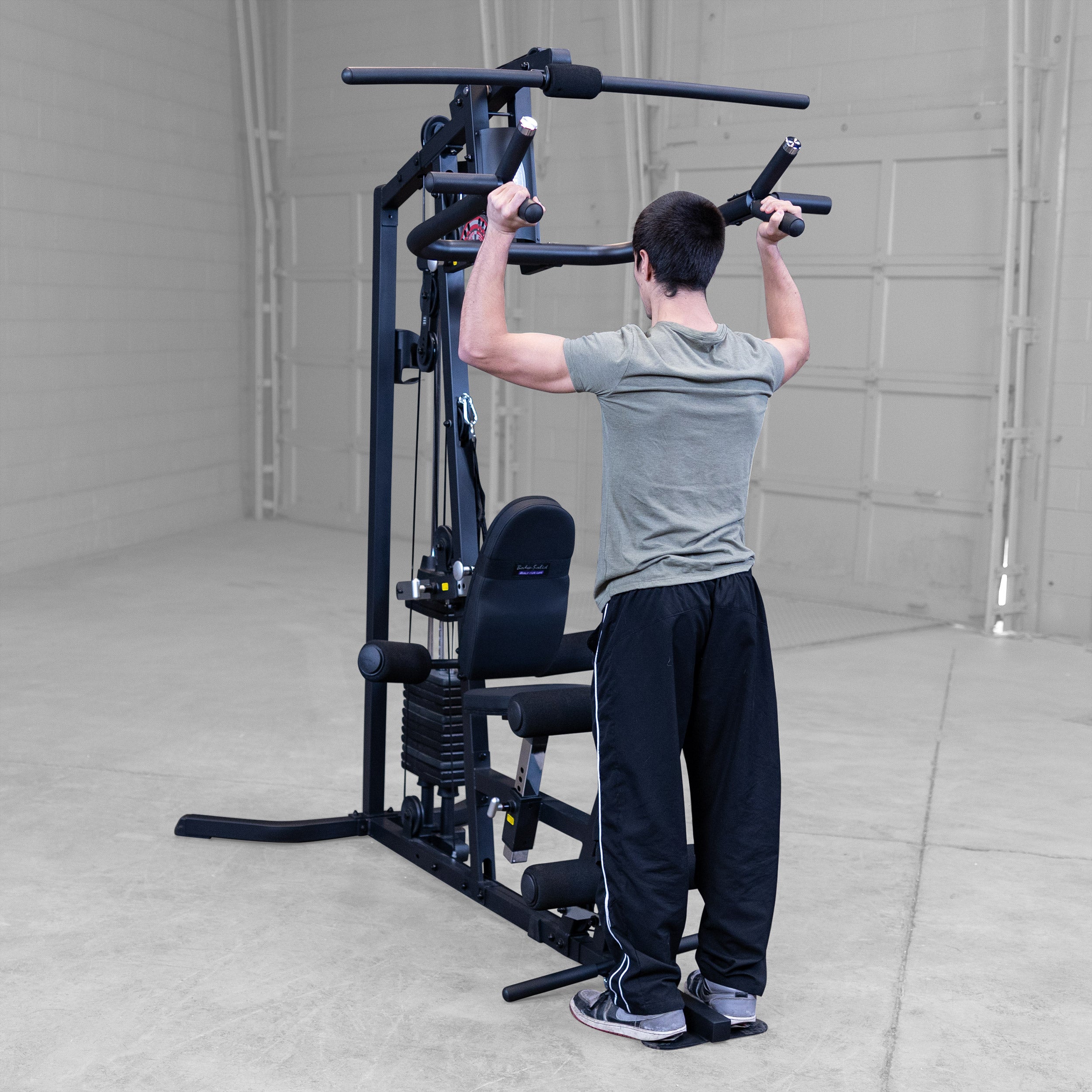 Person performing standing shoulder presses on the Body-Solid G3B multi station home gym to strengthen the shoulders and triceps