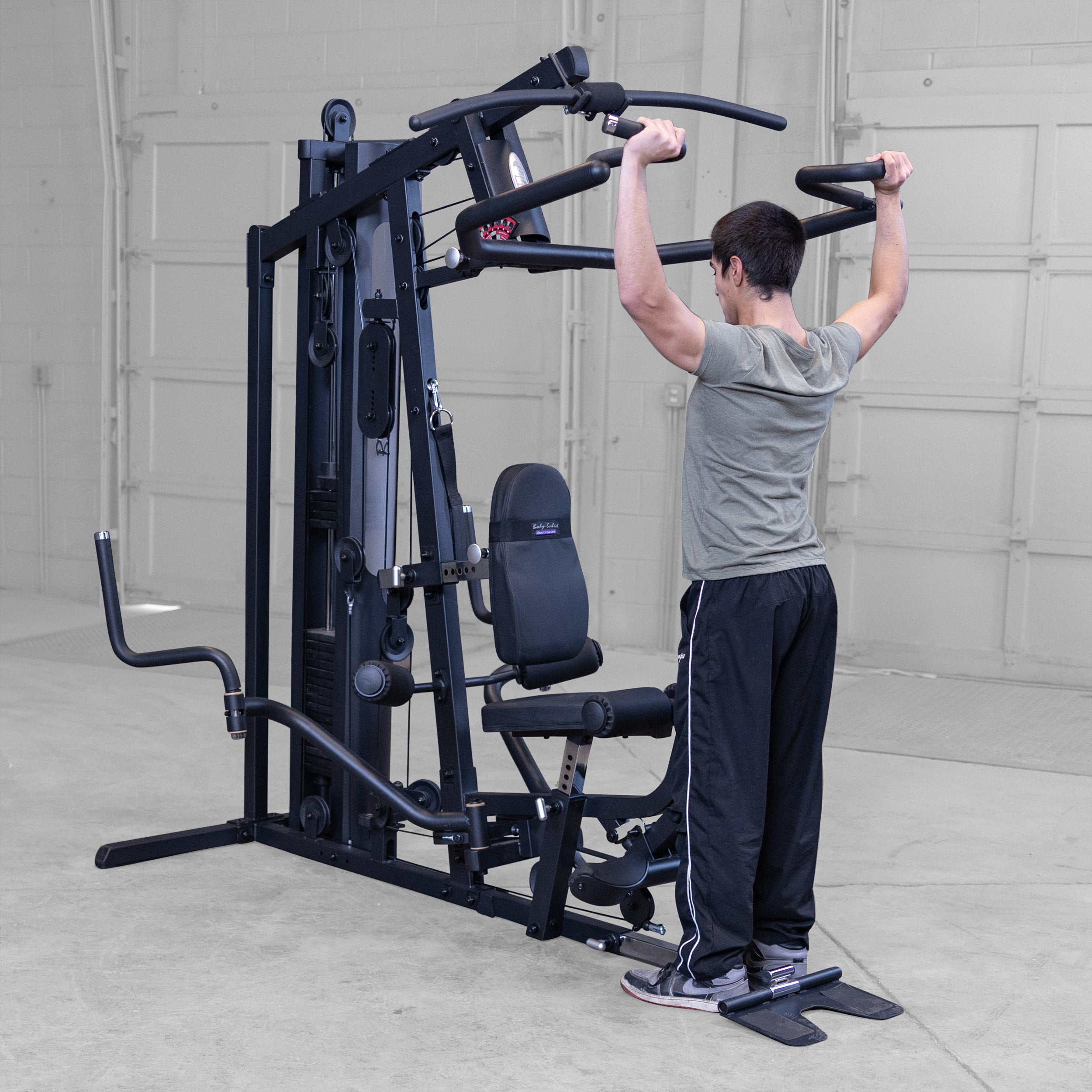 Person performing standing shoulder presses on the Body-Solid G5B multi station home gym to strengthen the shoulders and triceps