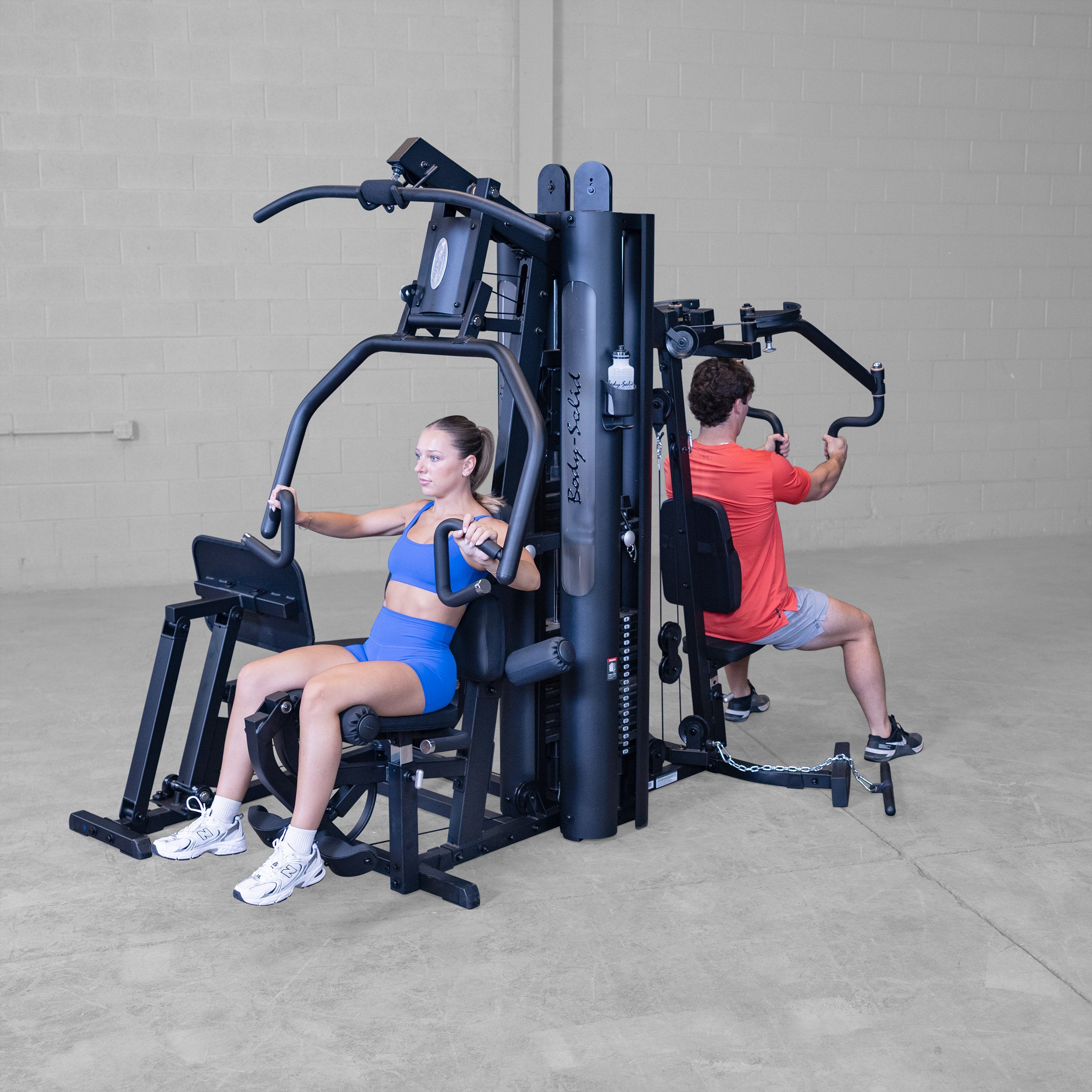 Two people training simultaneously on the Body-Solid G9B dual stack multi station home gym performing chest press and seated row exercises