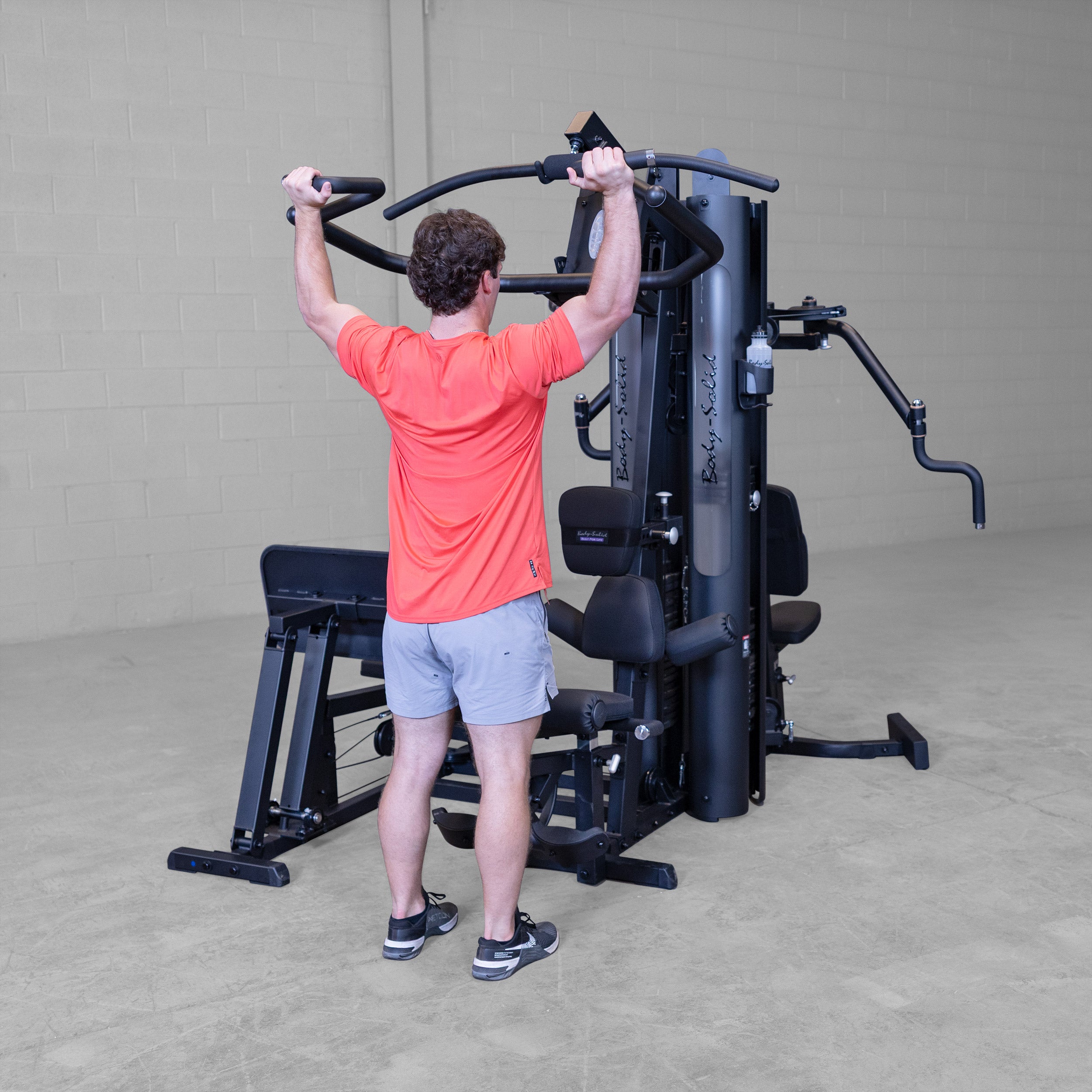 Person performing standing shoulder press exercise on the Body-Solid G9B dual stack multi station home gym using the Bi-Angular press arms