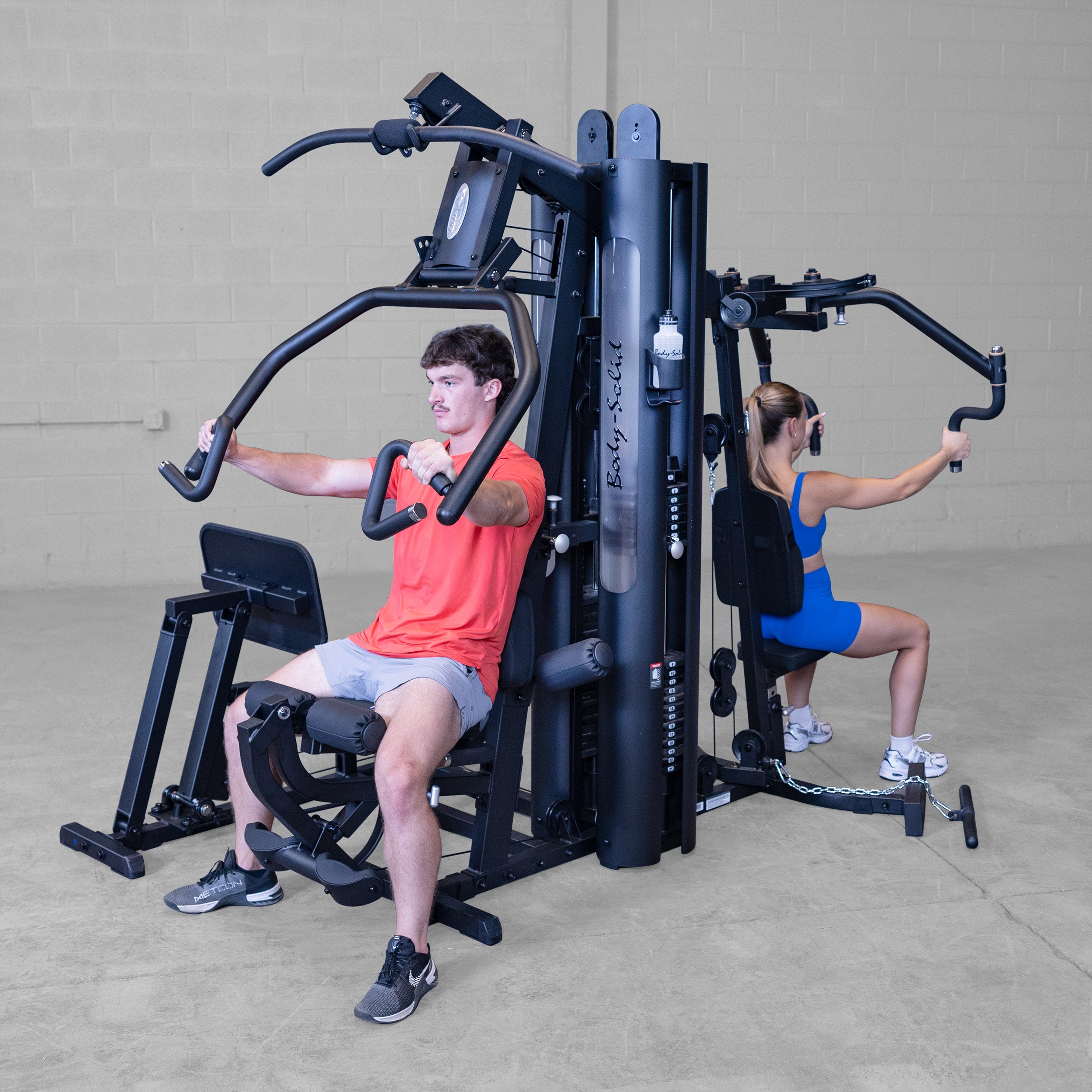 Two people training simultaneously on the Body-Solid G9B dual stack multi station home gym performing chest press and pec fly exercises