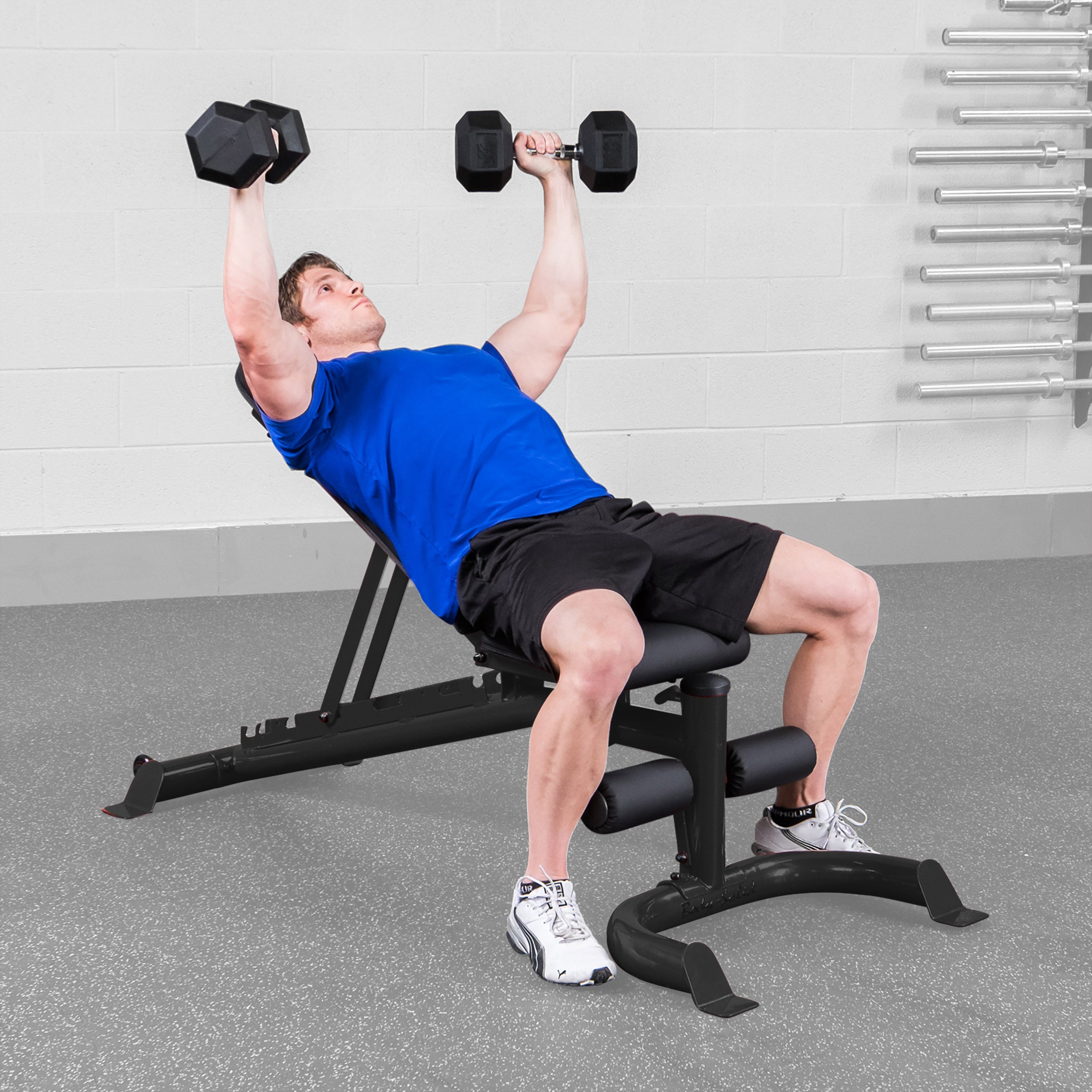 Person performing incline dumbbell press on Body Solid GFID100B adjustable weight bench in a home gym