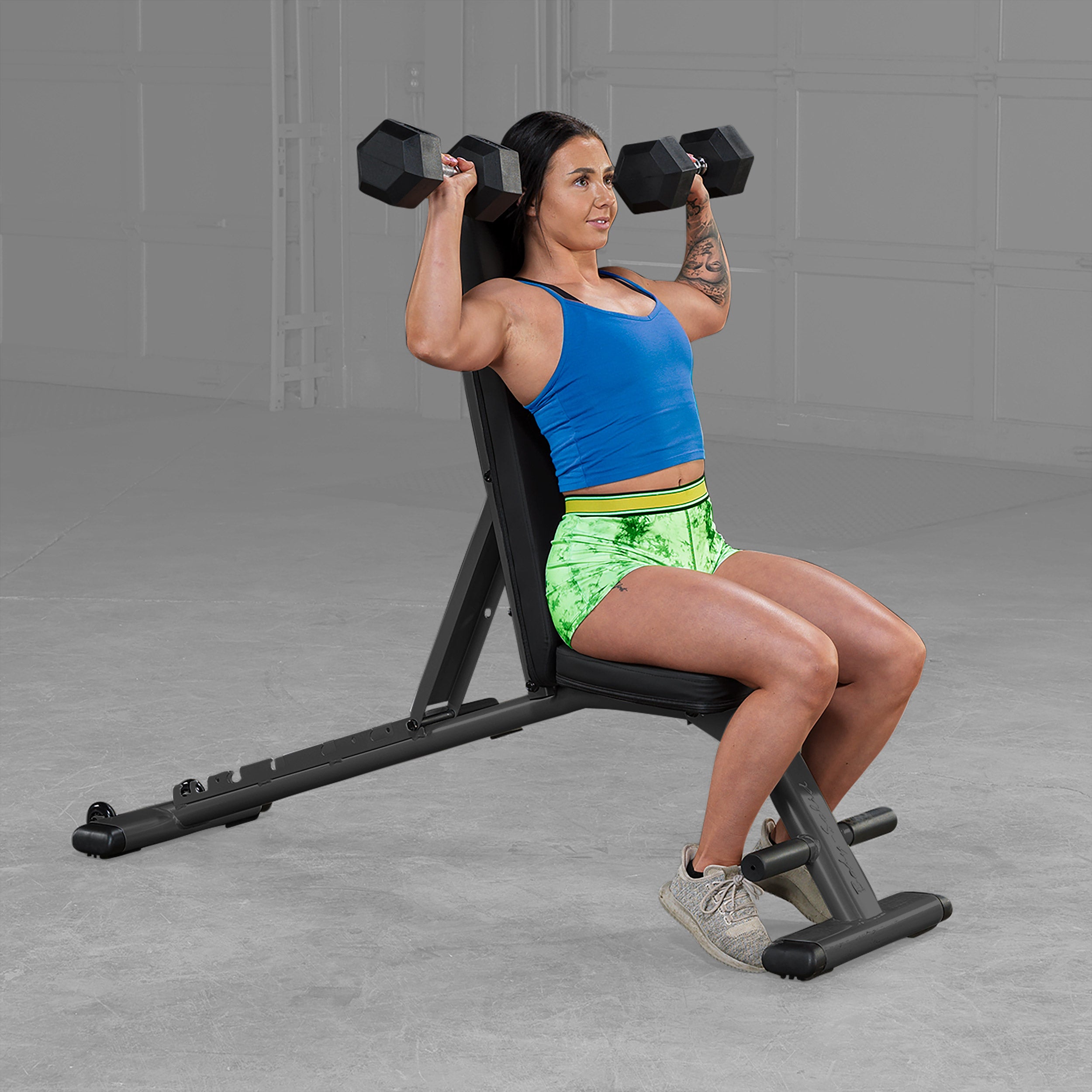 Person performing seated dumbbell shoulder press on Body Solid GFID225B folding adjustable weight bench in a home gym