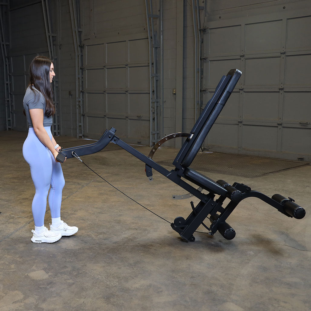 Person using the integrated transport handle and wheels to easily move the Body-Solid GLEG leg extension curl bench between workout and storage positions