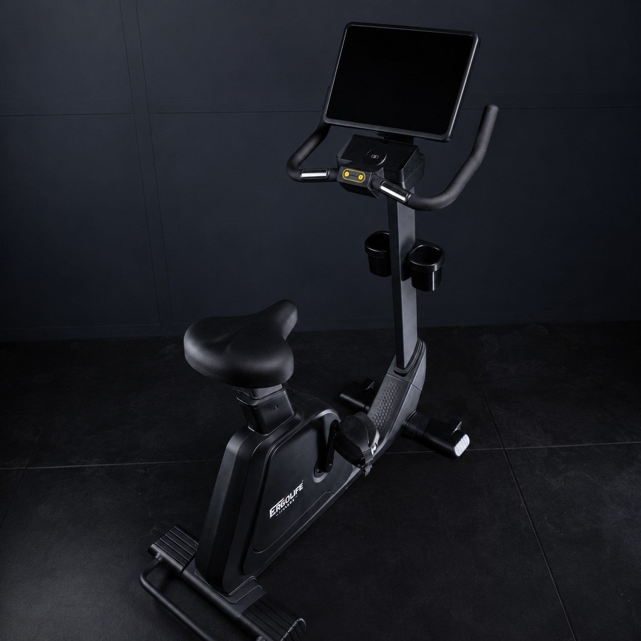 Close-up angled view of the ERGOLIFE BU201E upright exercise bike featuring the LCD display, tablet holder, adjustable seat, and magnetic resistance system