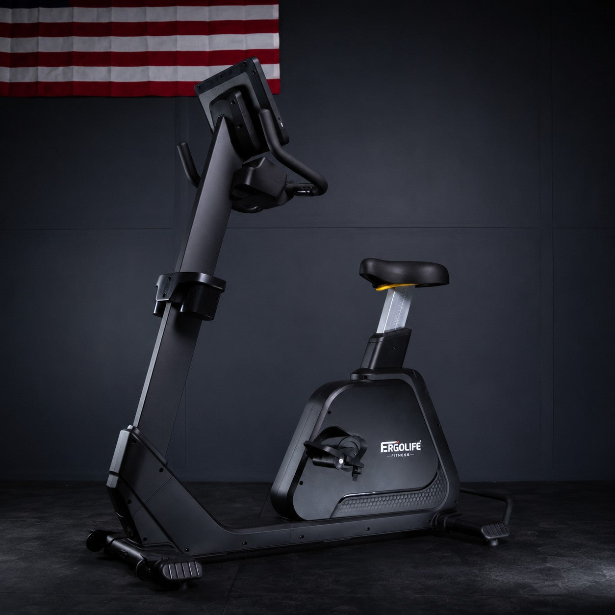 ERGOLIFE BU201E upright exercise bike with magnetic resistance in a modern gym setting, featuring an adjustable seat, LCD display, and tablet holder