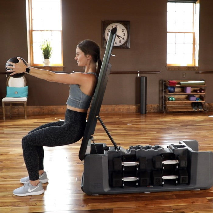 Woman performing medicine ball exercise on FITBENCH FREE adjustable workout bench