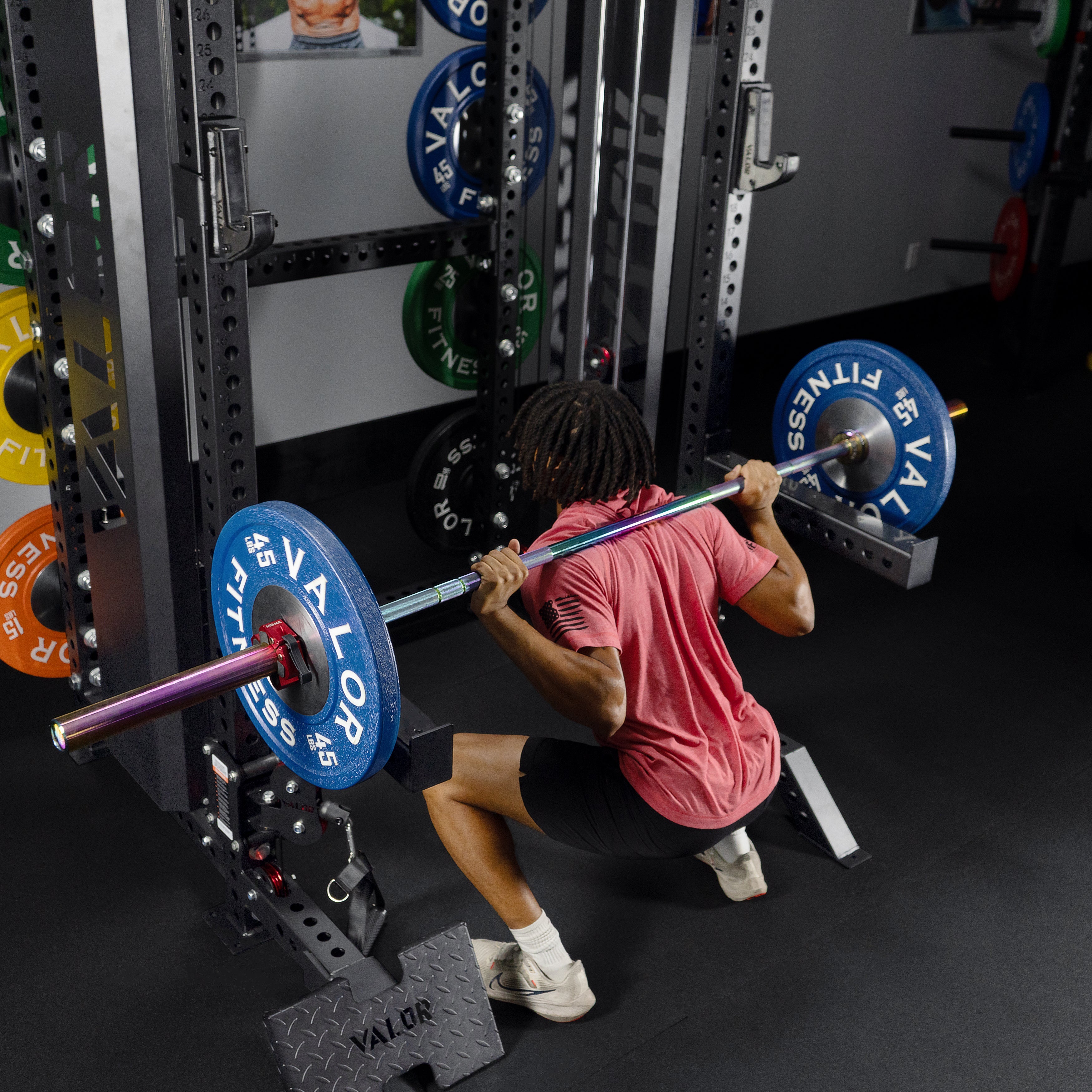 Athlete performing barbell back squats on the Valor Fitness BD-83 functional trainer power rack with safety spotter arms and weight plate storage pegs